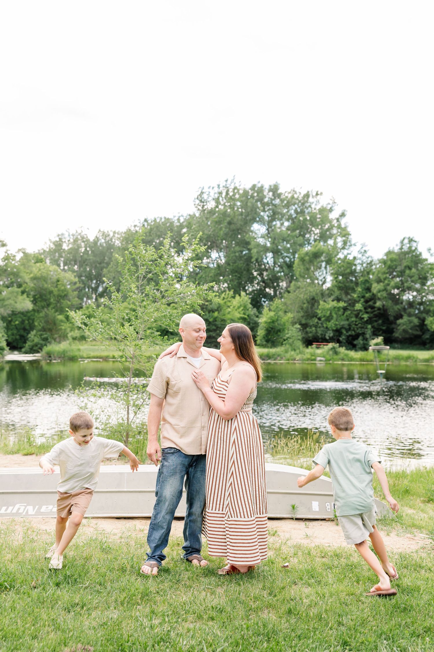 Parents holding hands with two boys running nearby during a playful Crystal Lake family photography session by the water.