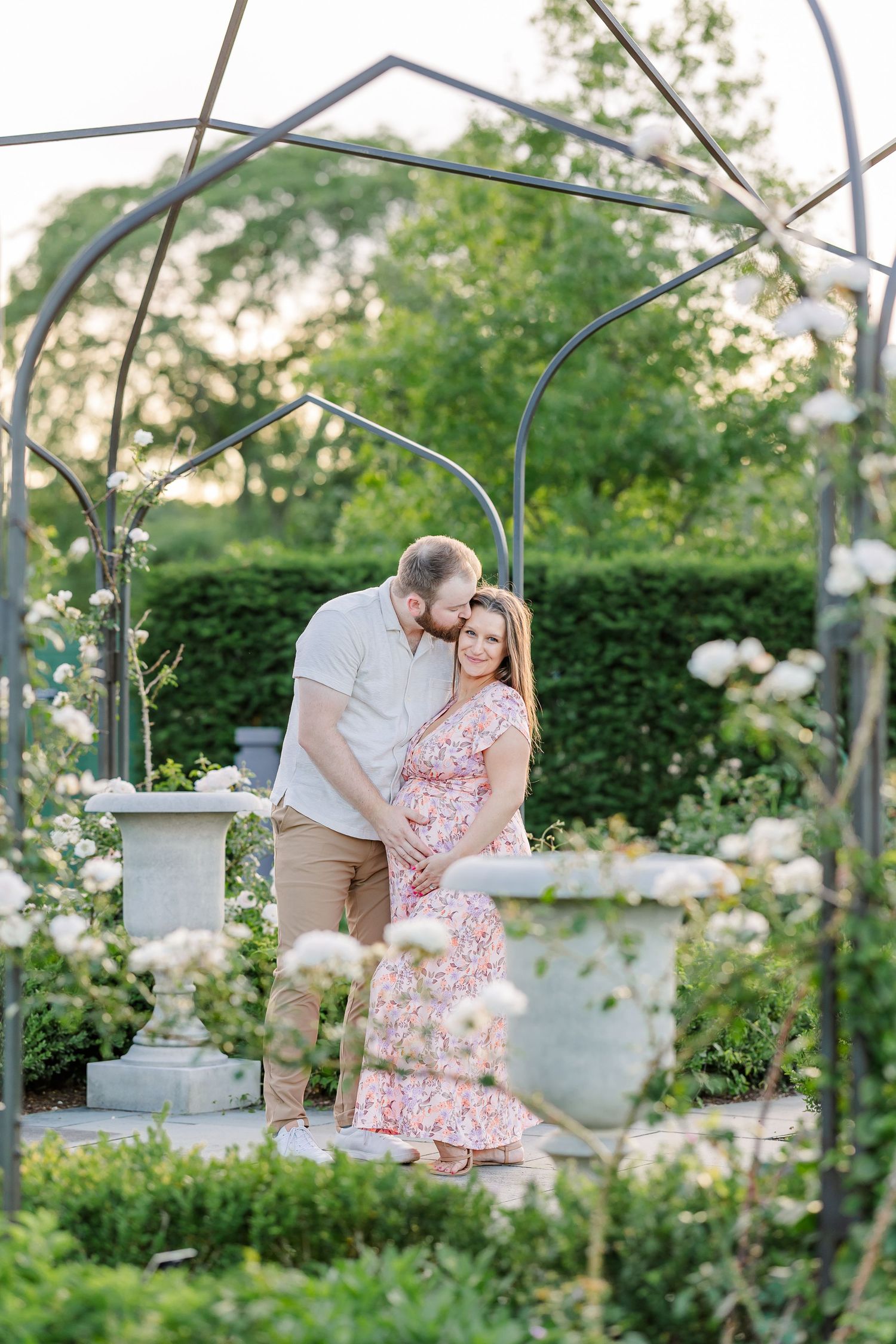 Expecting parents cuddling near a garden arch during their Cantigny Park maternity photos in Wheaton Illinois