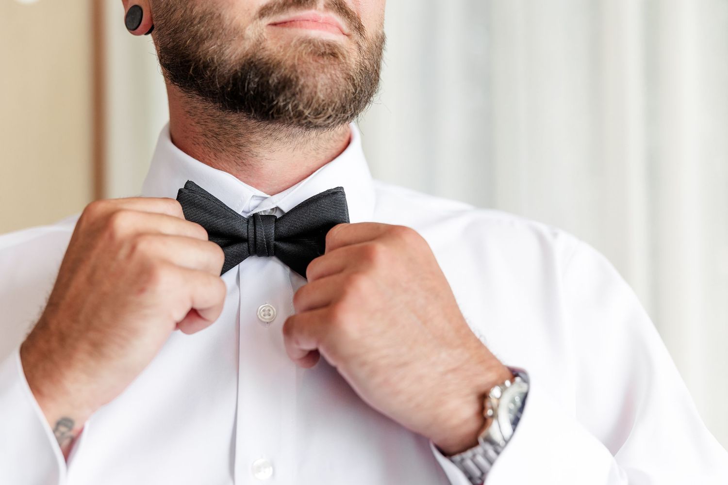 Groom adjusting black bow tie on white dress shirt, close-up wedding preparation photo.