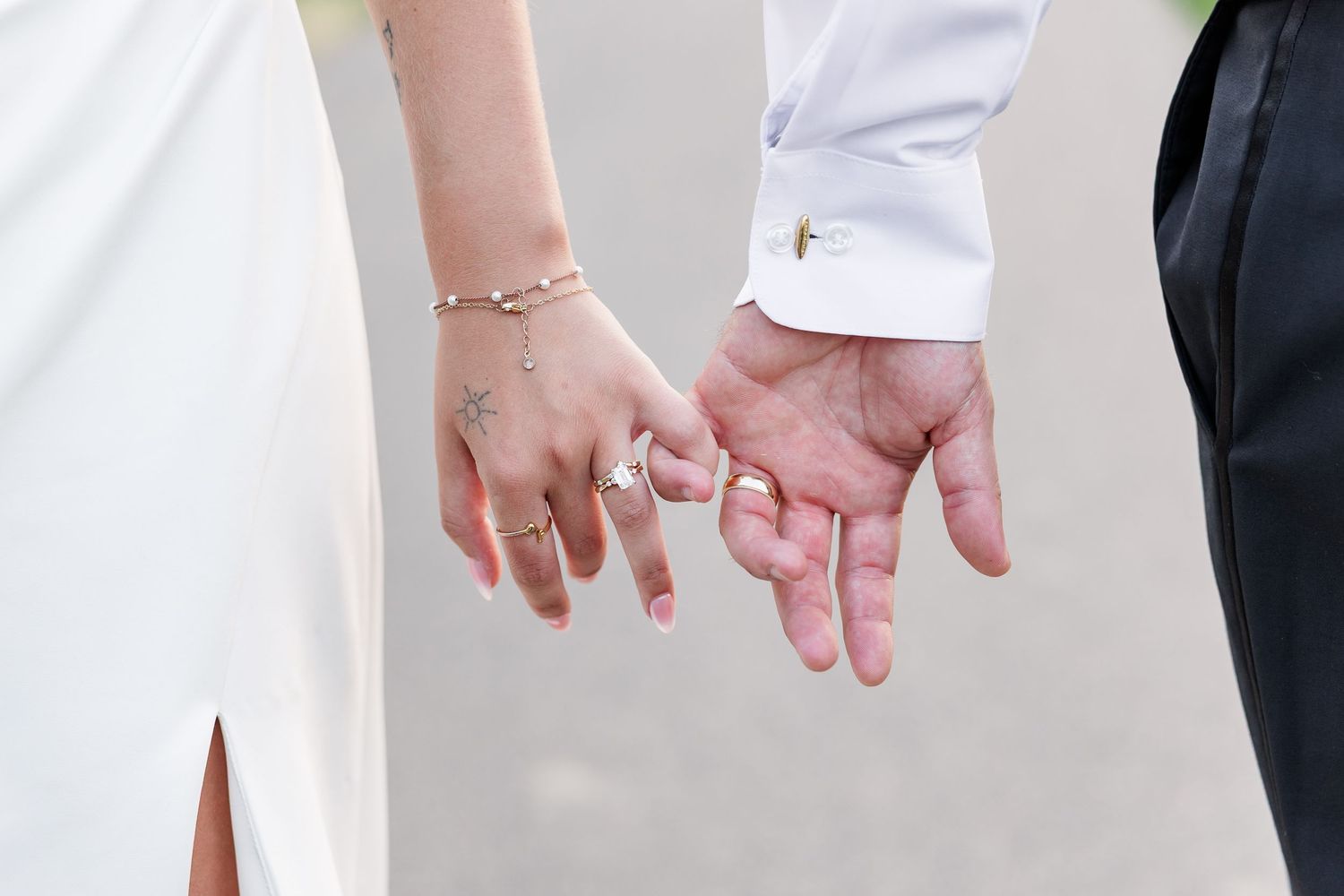 Close-up of bride and groom holding hands showing wedding rings, tattoos, and cross cufflink detail.