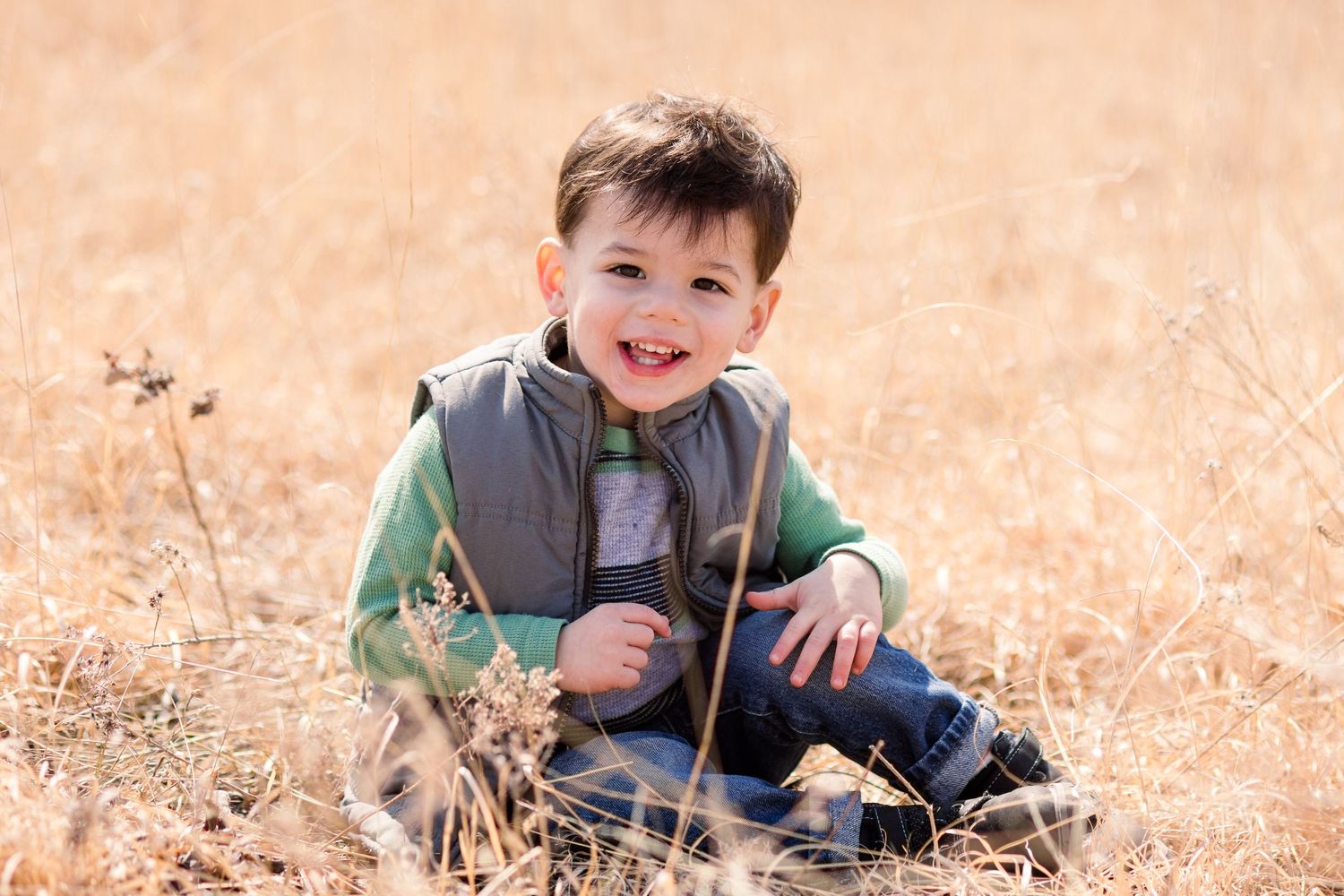 Young person sitting among tall golden grass in outdoor setting.