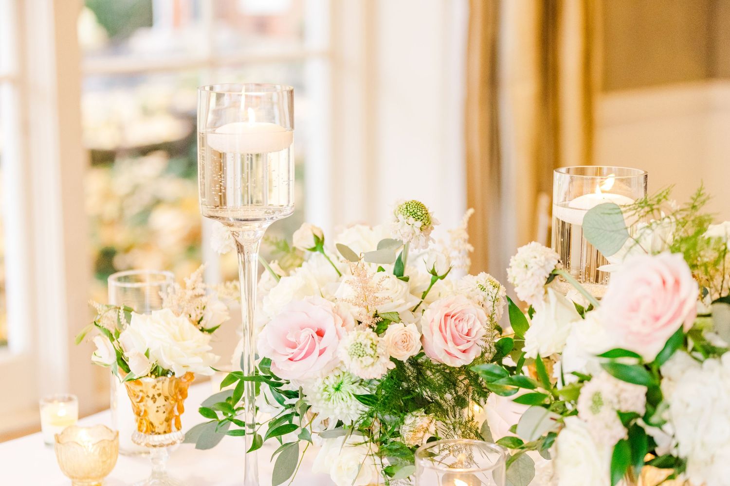 Wedding table centerpiece with pink roses, white flowers and champagne glasses in soft natural light.