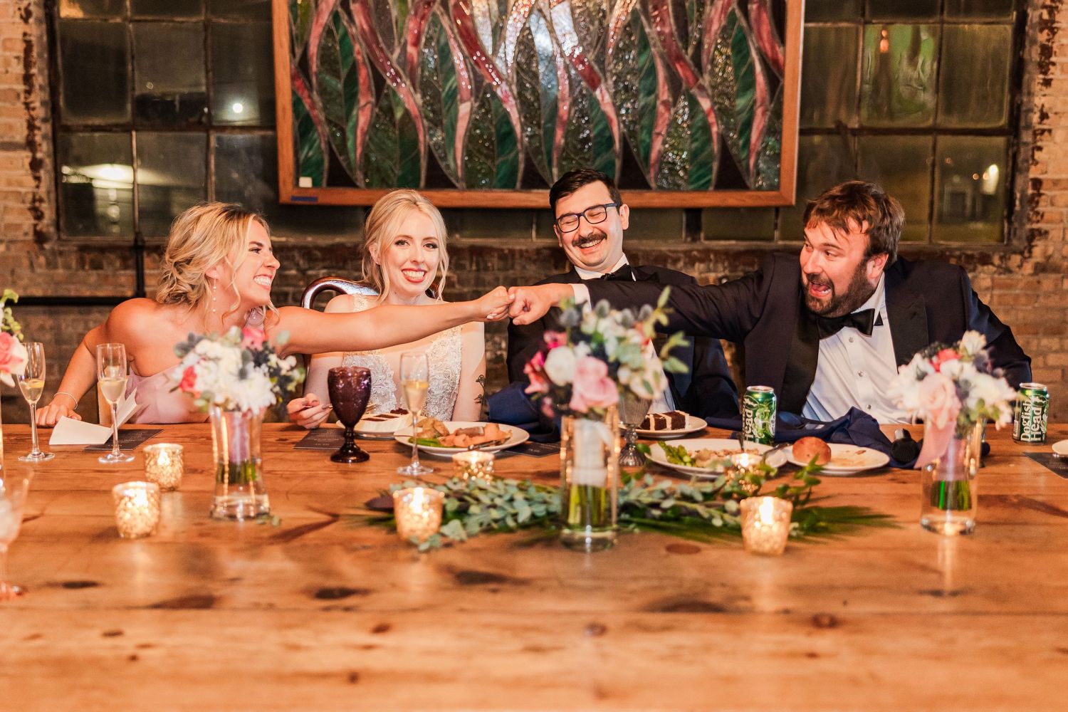 Wedding reception dinner with guests sharing laughs at rustic wooden table.