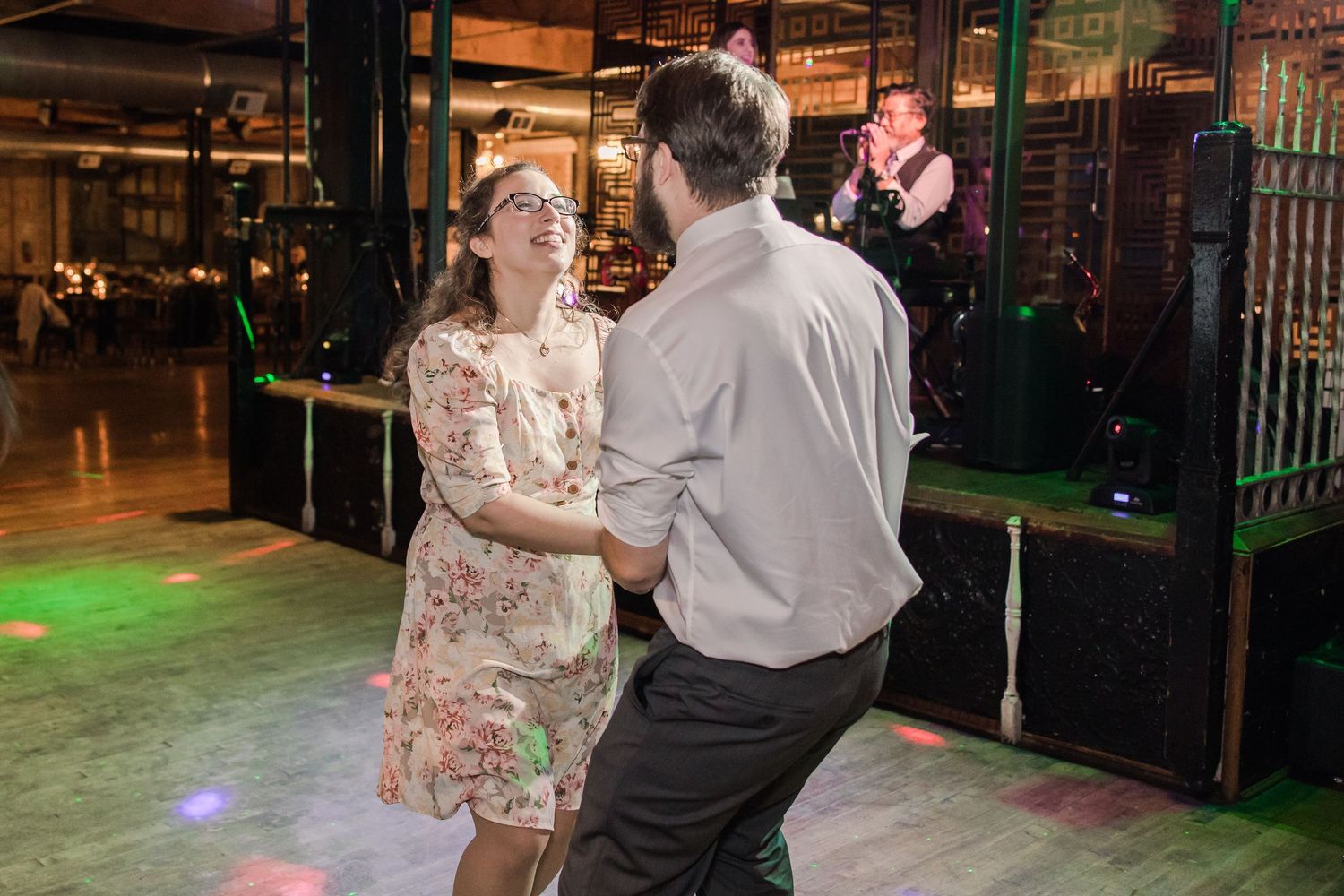 Couples dancing together at a wedding reception in an industrial-style venue with colored lighting.