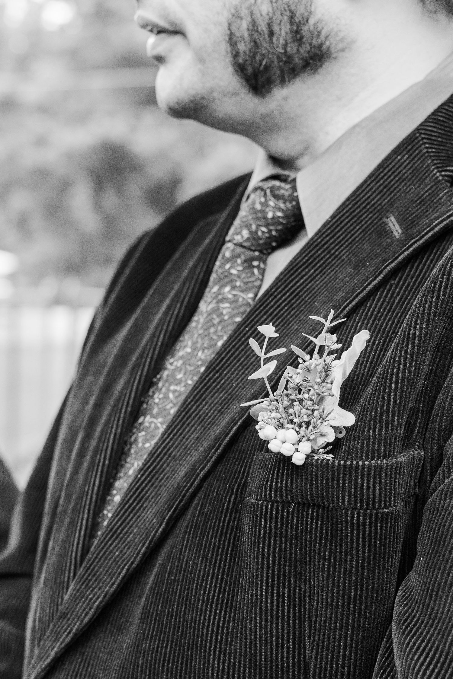 Close-up black and white detail of groom's boutonniere on pinstripe suit lapel.
