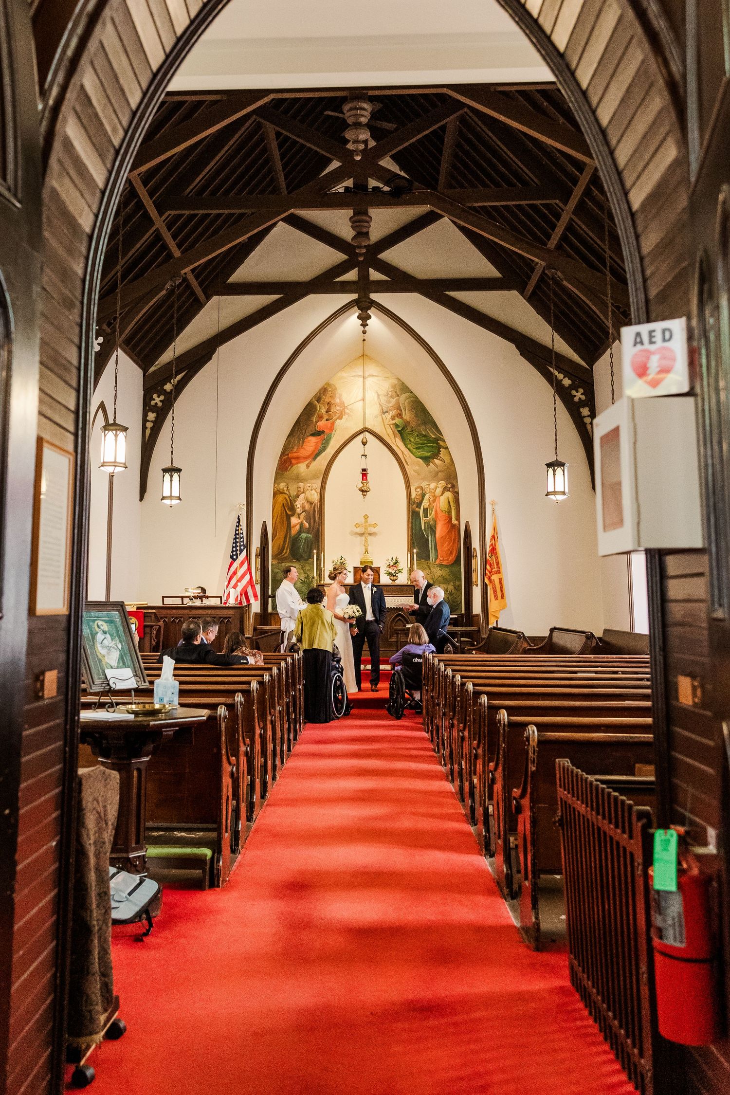 Church interior with vaulted ceiling, wooden pews, and red carpet leading to ornate altar.
