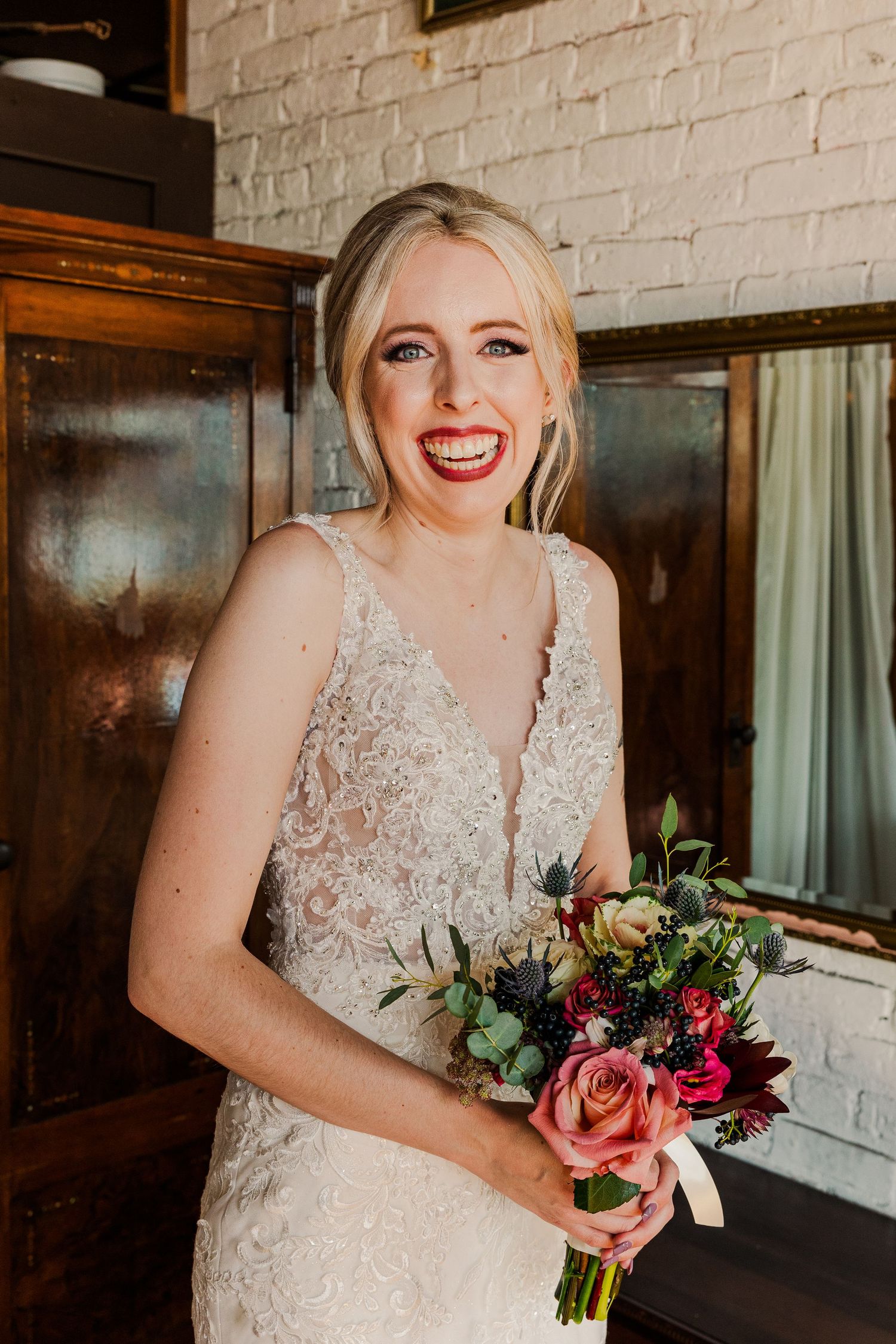 Joyful bridal portrait with vibrant bouquet against rustic brick backdrop.