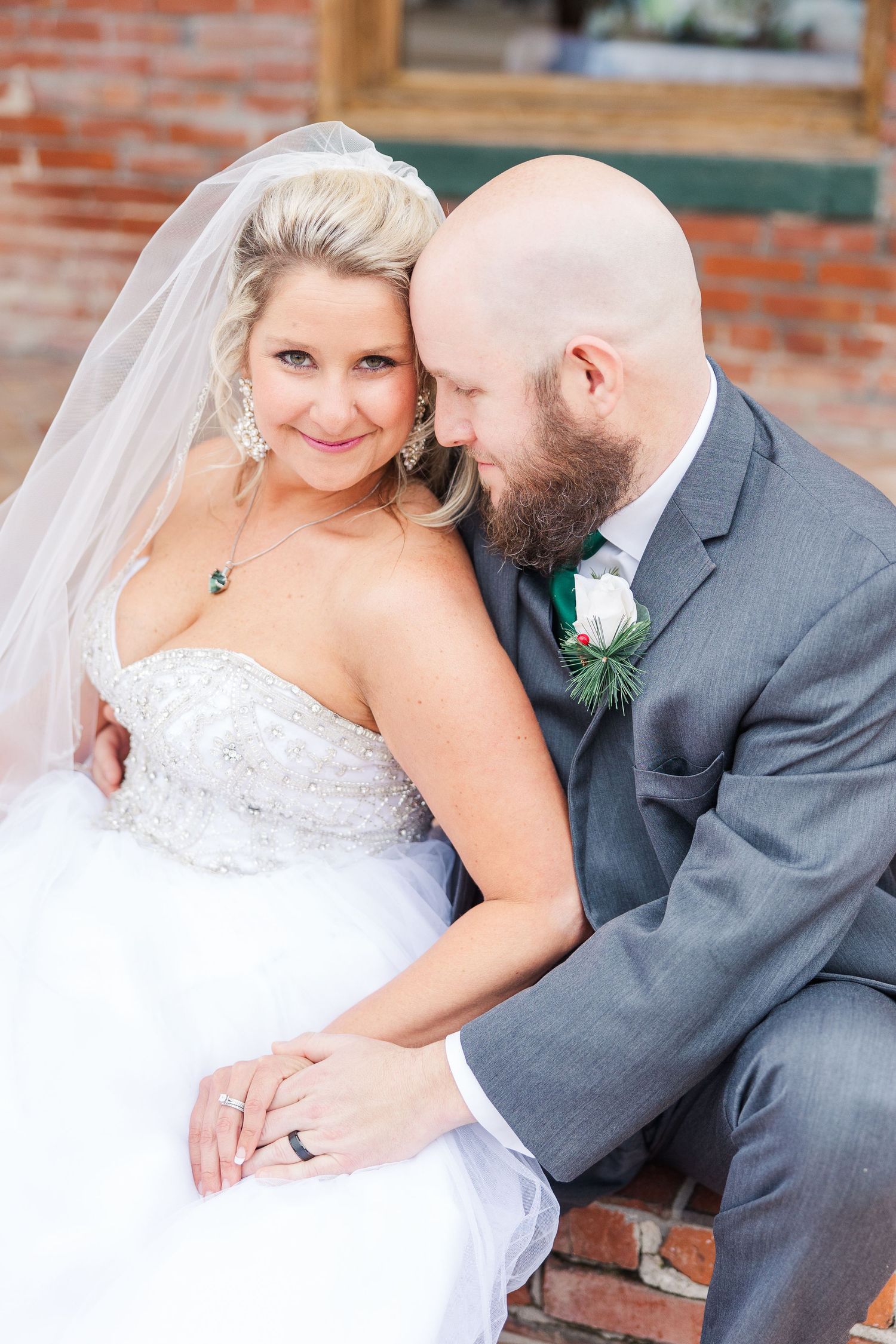 Romantic wedding portrait featuring close embrace against rustic brick background.