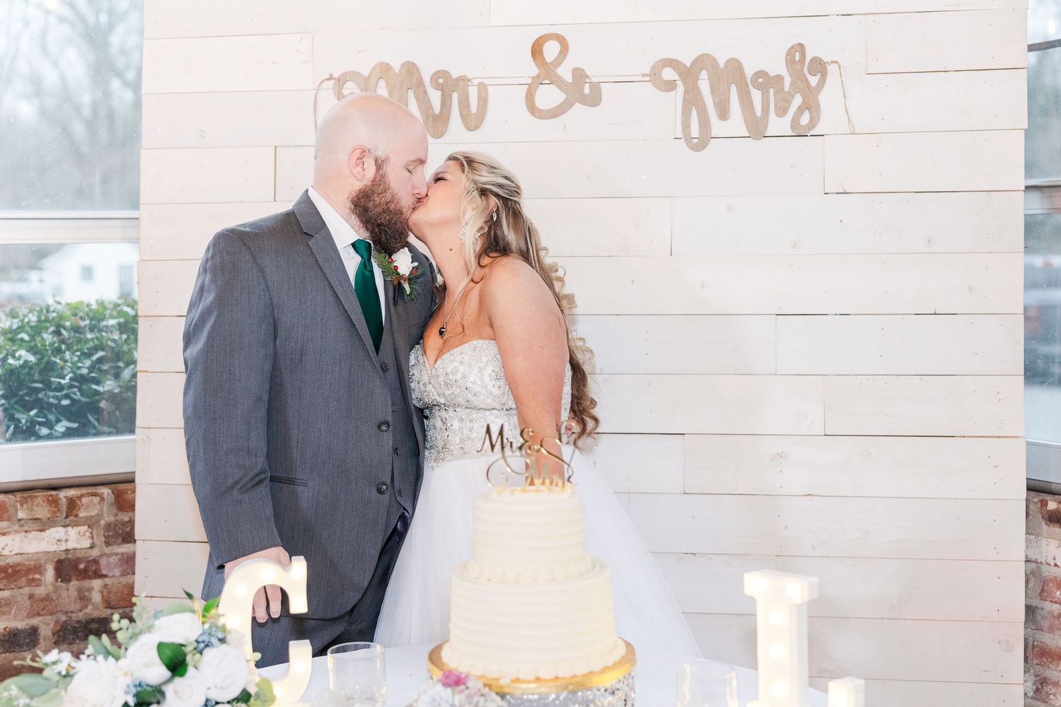 Newlyweds sharing intimate moment after cake cutting with Mr & Mrs sign in background.