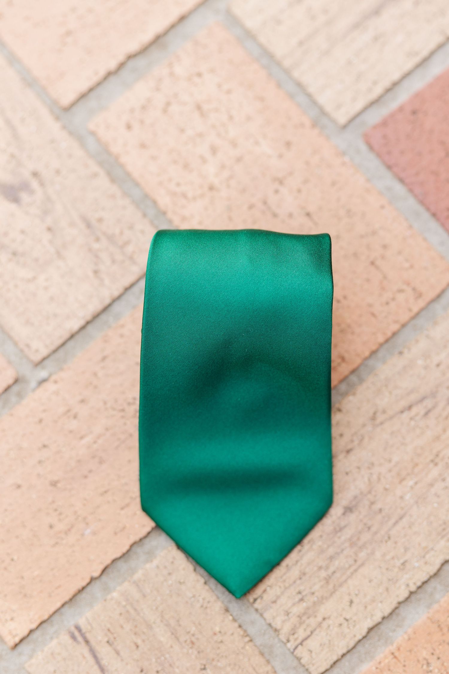 Emerald green silk tie lying on beige brick or stone flooring.