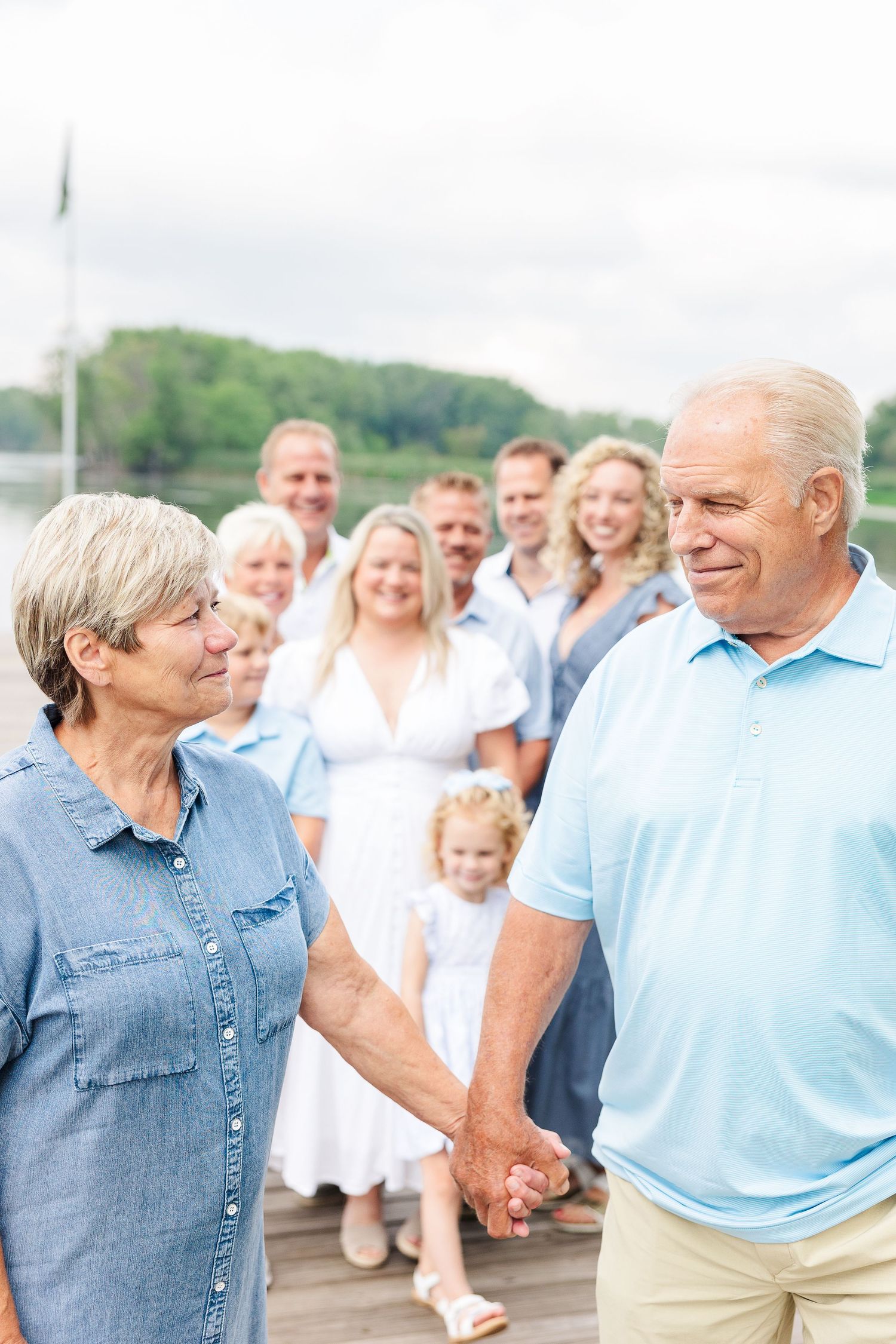 A tender moment shared between a couple holding hands on a dock with family gathered behind them.