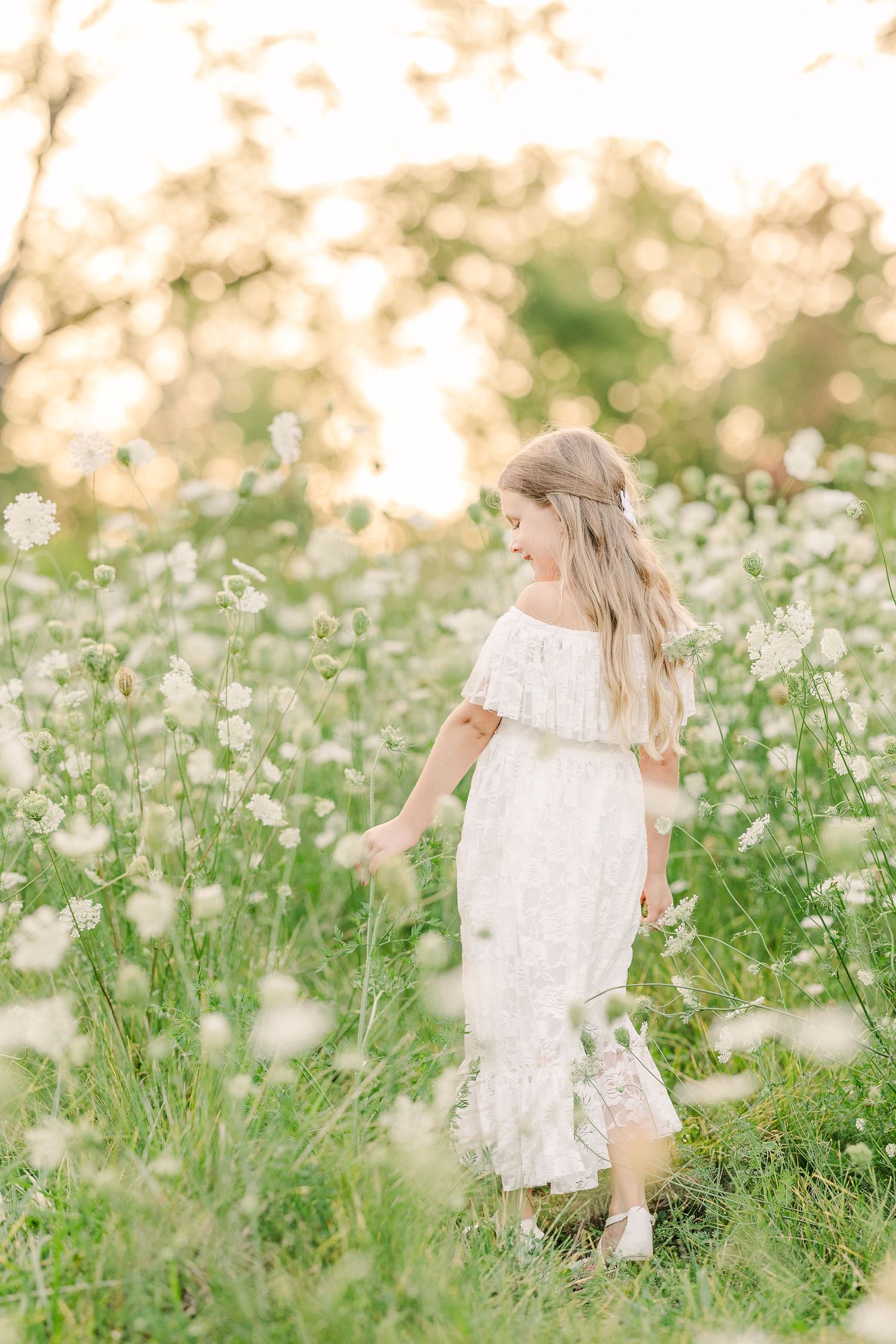 A white lace dress stands out against wildflowers in a dreamy summer meadow at golden hour.