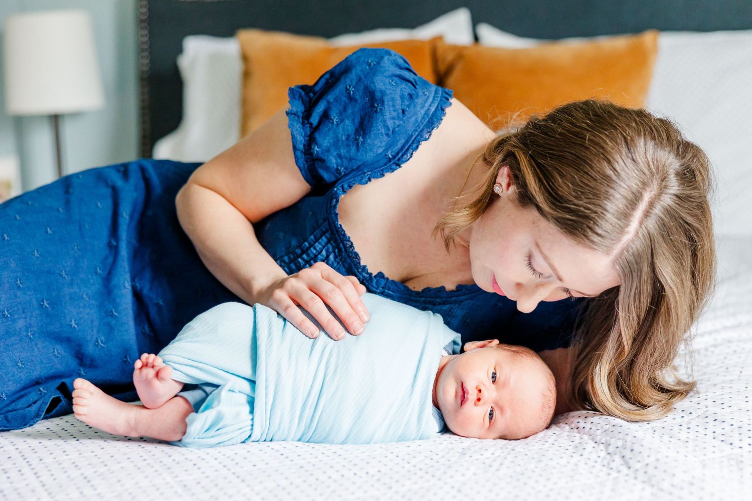 Mother snuggles newborn son on bed during in-home lifestyle newborn session in Crystal Lake, Illinois