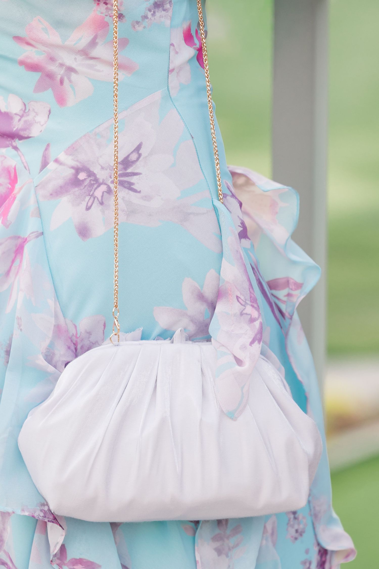 White ruched clutch purse with gold chain strap against a light blue floral dress.