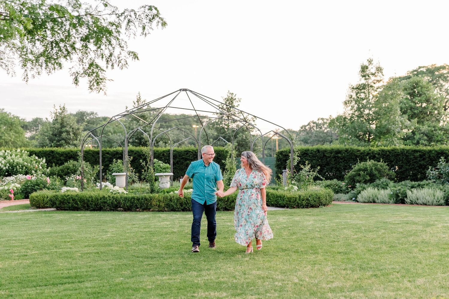 Happy couple holding hands and walking through a lush green garden on a sunny day.
