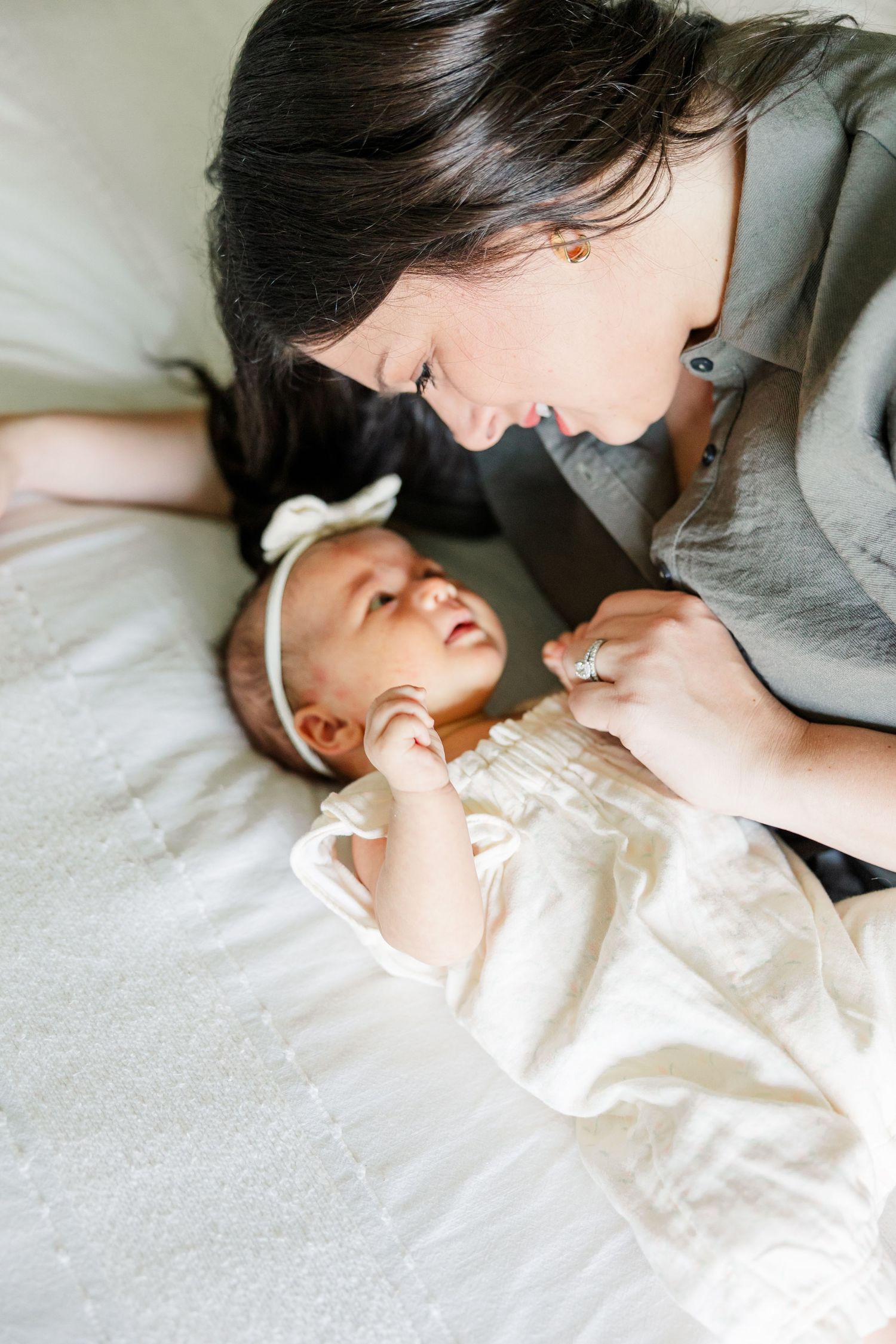 Mom smiling over newborn baby girl on the bed during a sweet in-home newborn photography session