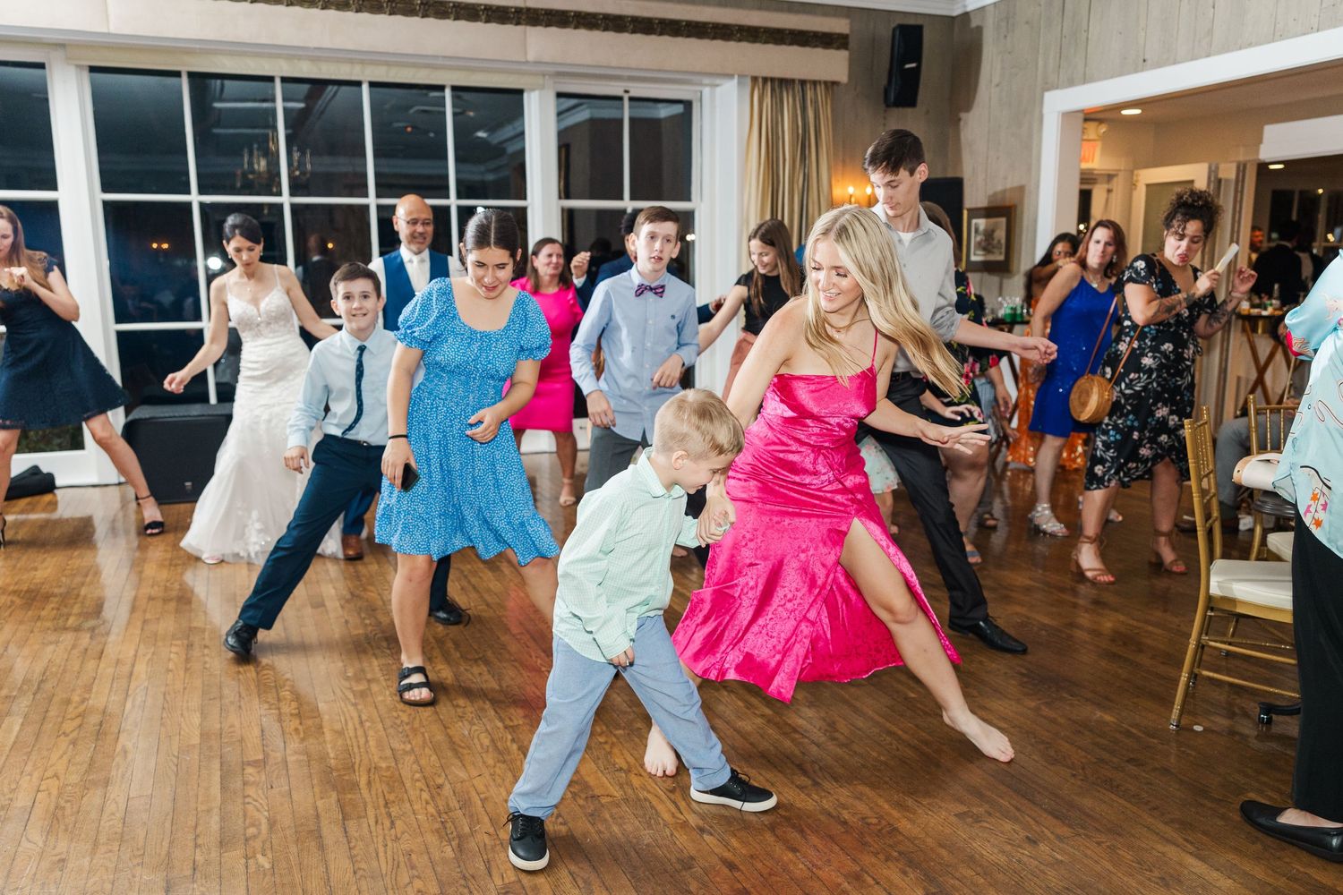Wedding guests dancing enthusiastically on a wooden dance floor with bright dresses and festive energy.