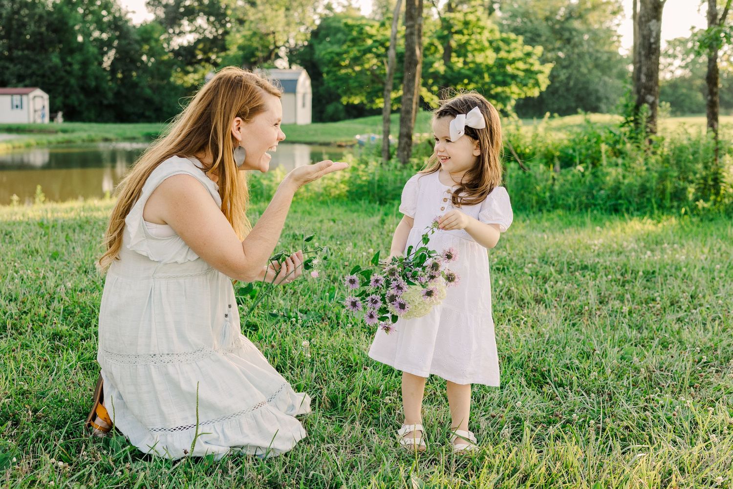 Two people in white dresses playing with flowers in a green field.