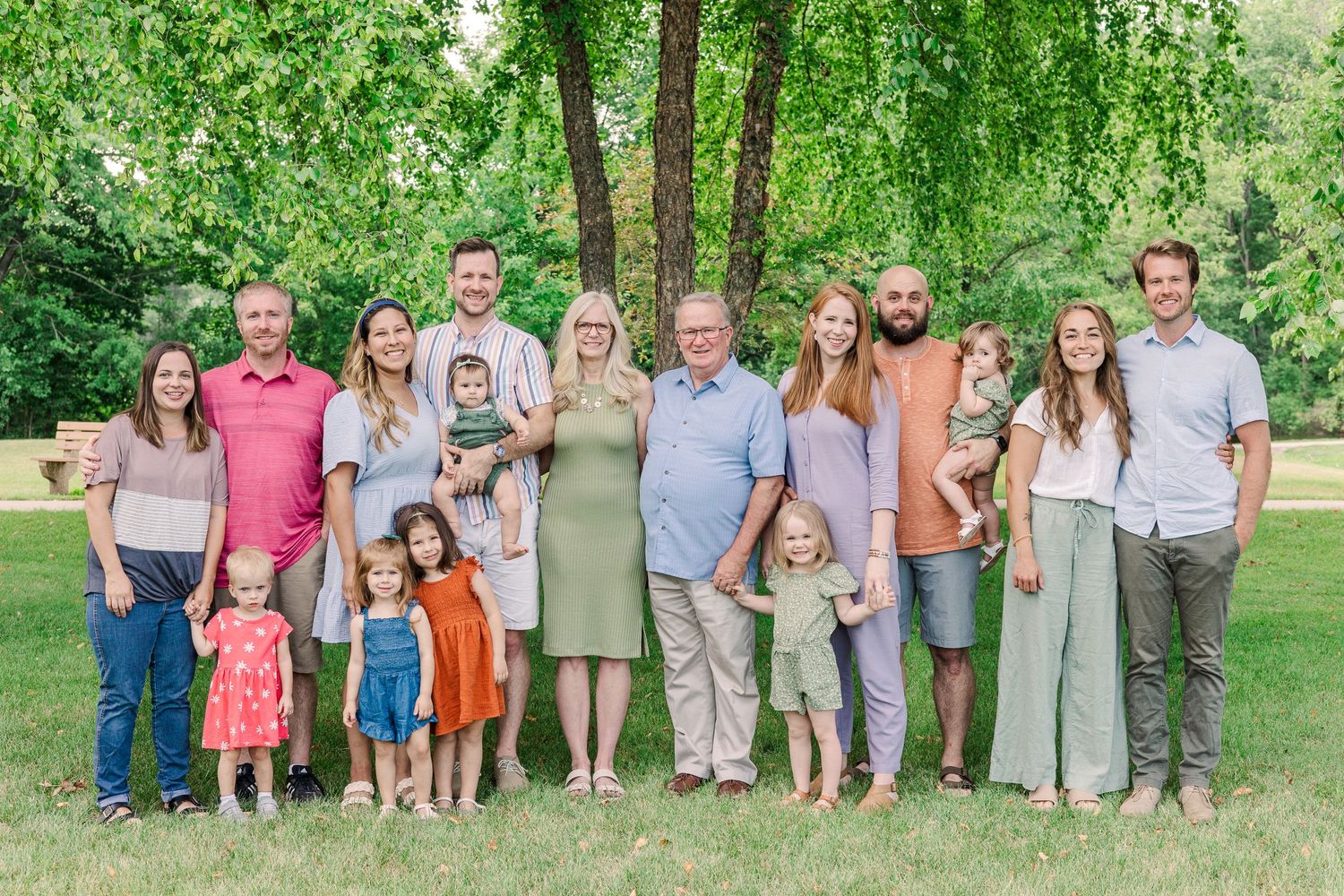 Extended family group portrait with multiple generations posed together under green trees.
