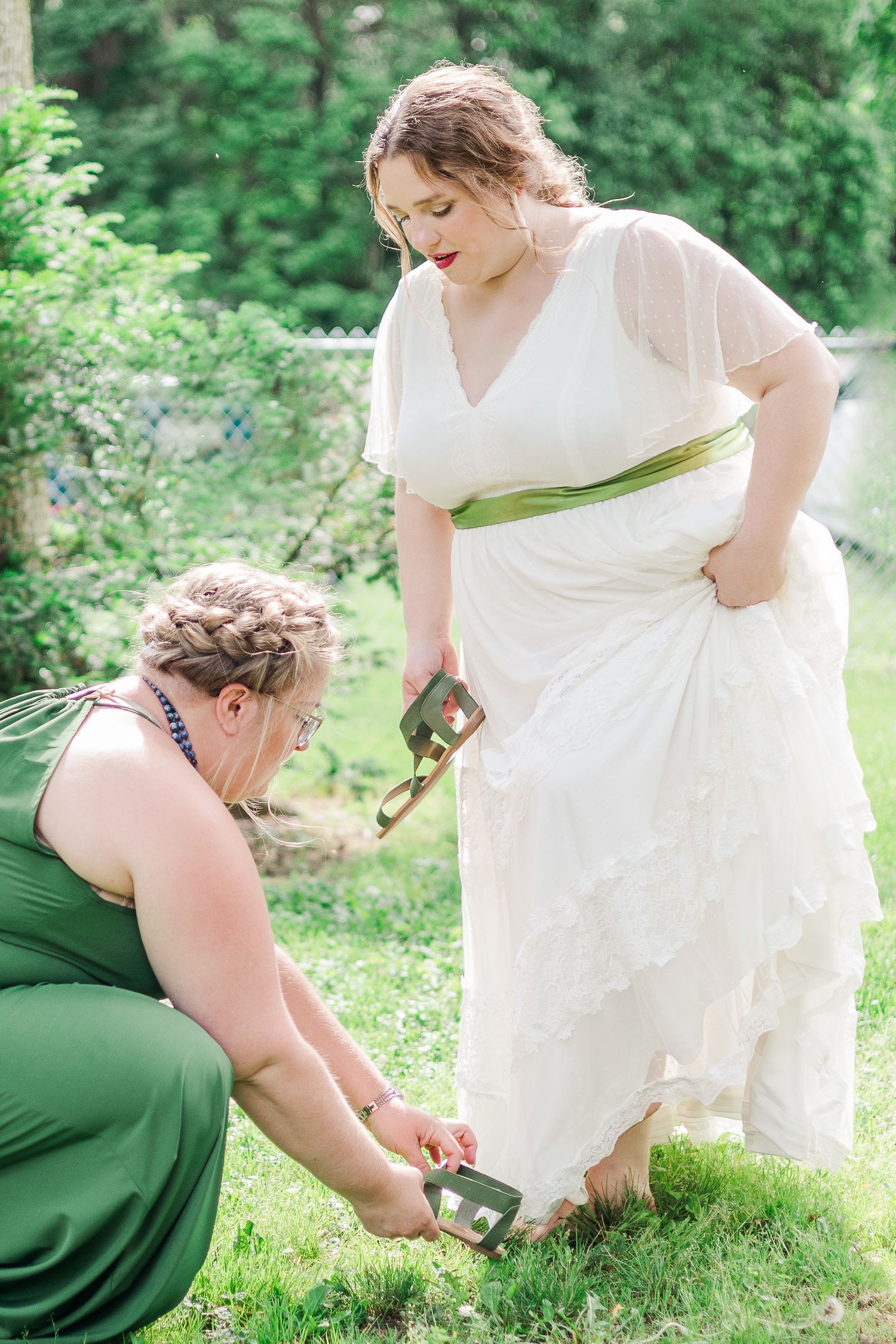 Two people in formal attire adjust shoes on grass during outdoor event.