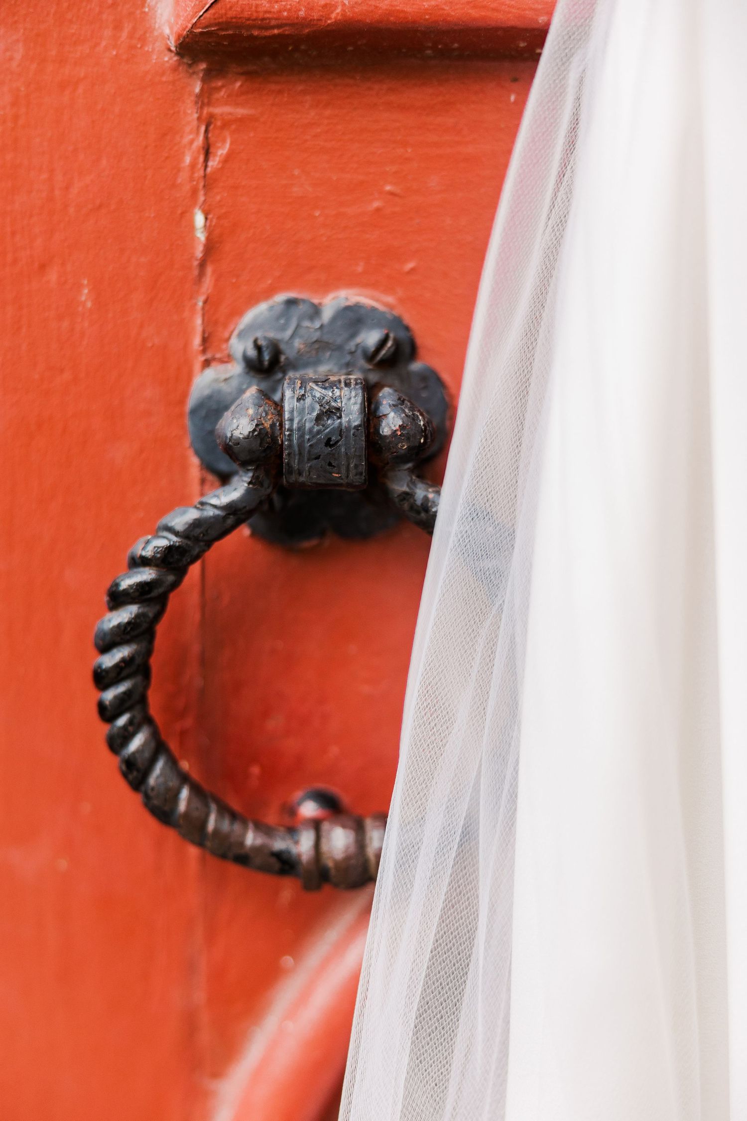 Vintage wrought iron door knocker mounted on a bright orange painted door.