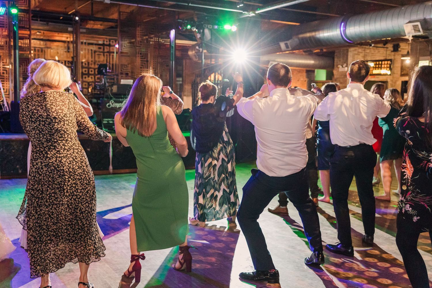 Wedding guests dancing enthusiastically on a dimly lit dance floor with colored lighting.