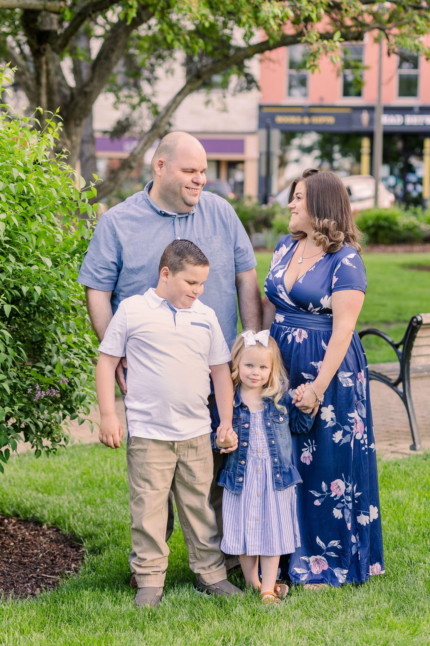 A family poses together on green grass with brick buildings in the background on a sunny day.