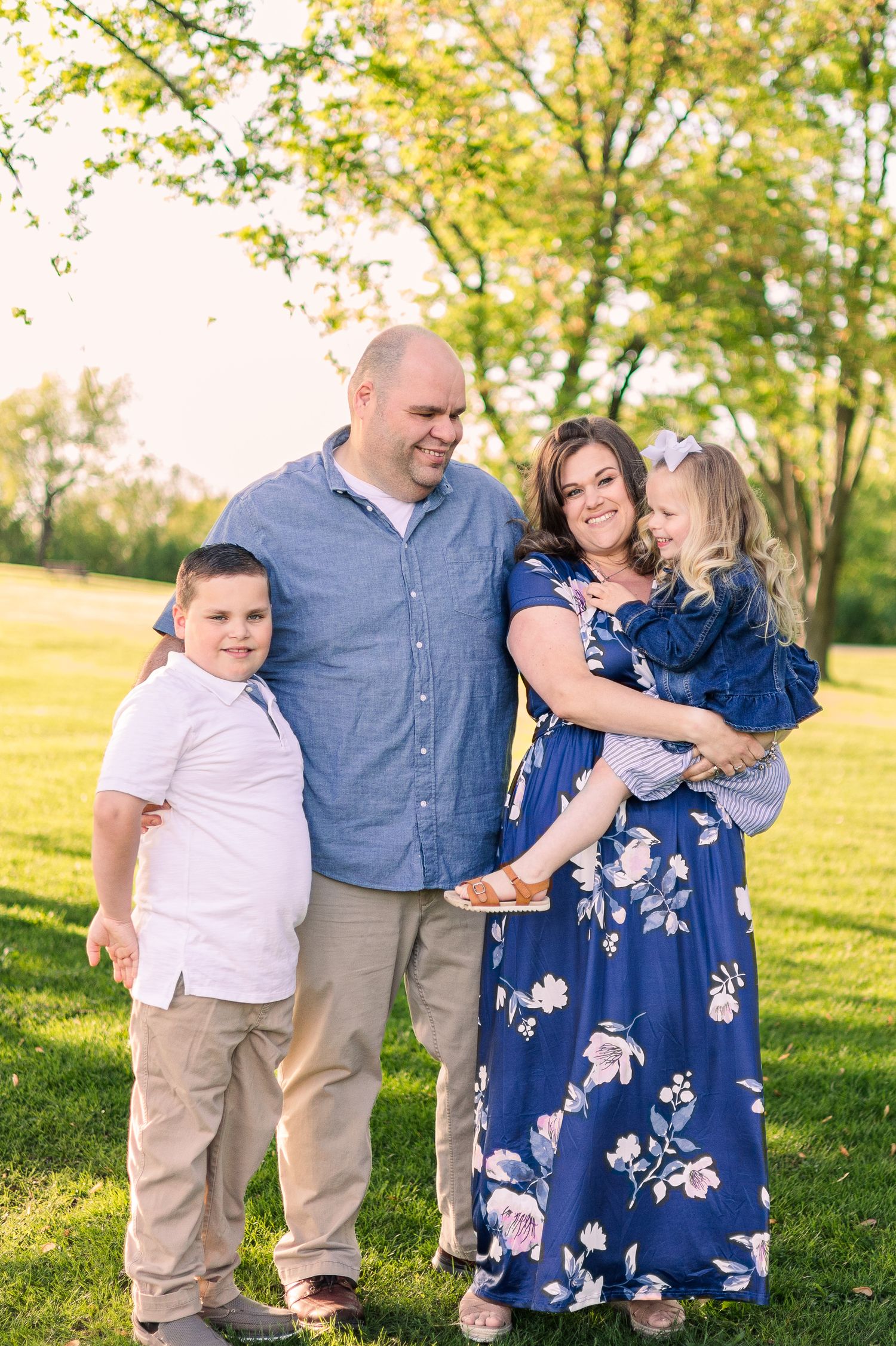Family group photo standing together in a sunlit park with trees in background.