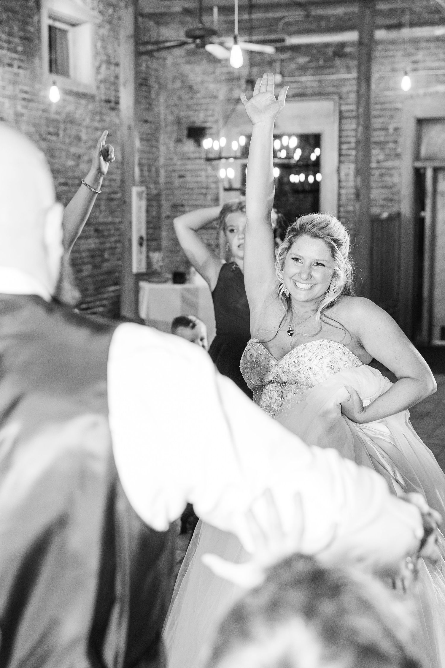 Dancing at a rustic wedding reception with exposed brick walls and pendant lighting.