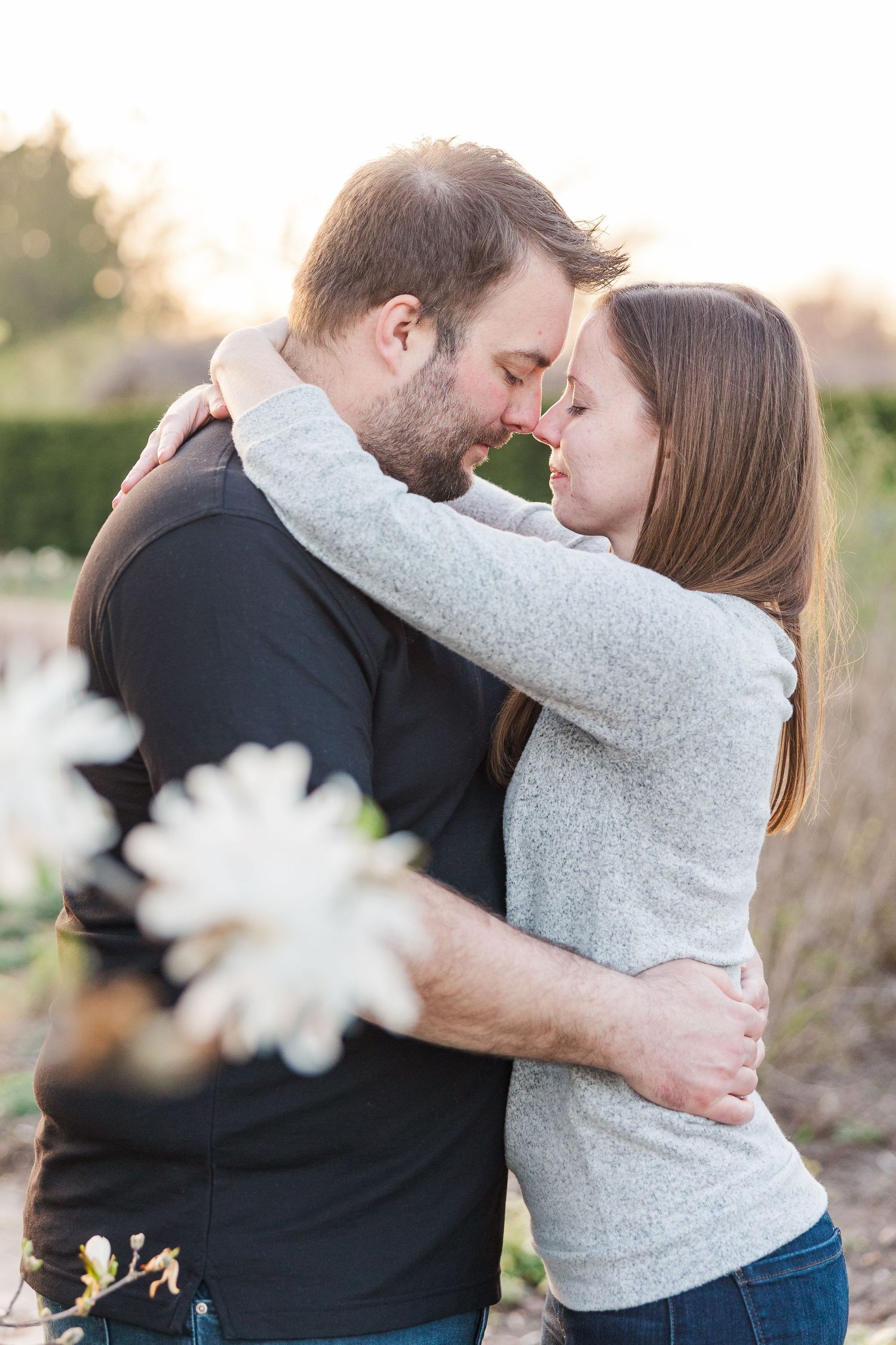 Intimate embrace captured in soft natural lighting with flowers in foreground.