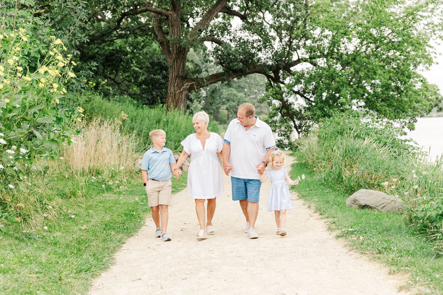 A family walks together on a sunny nature trail surrounded by lush summer greenery.