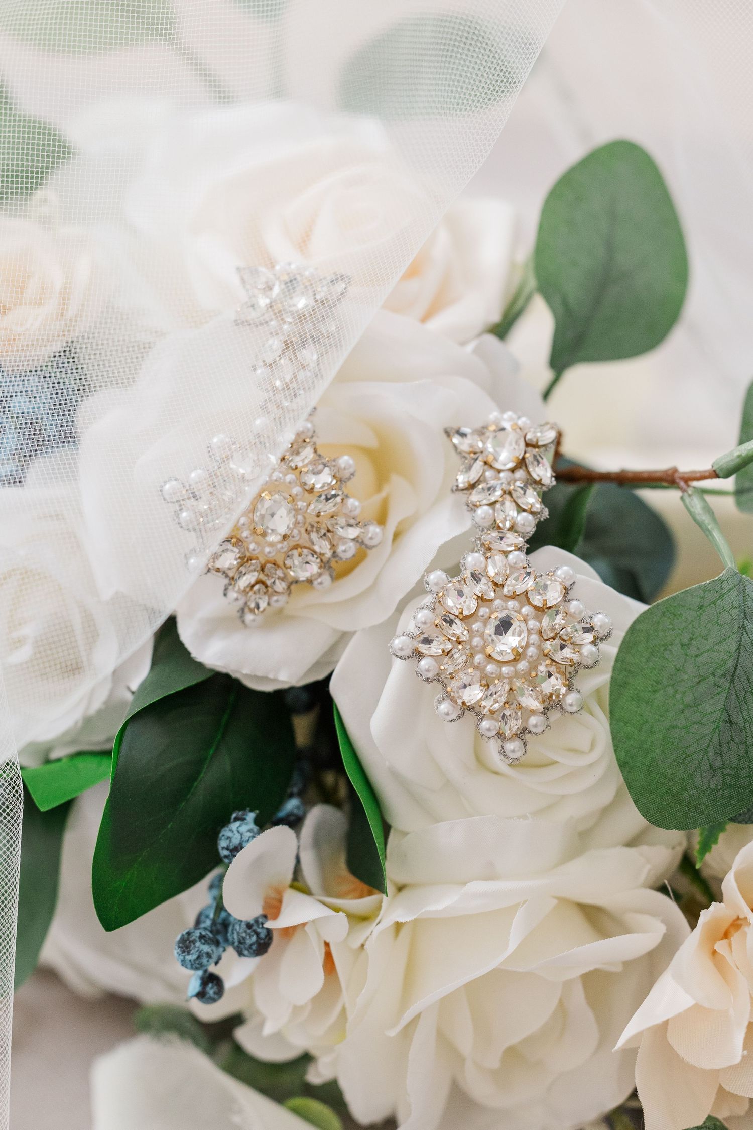 White roses with crystal brooches and eucalyptus leaves create an elegant bridal accessory arrangement.