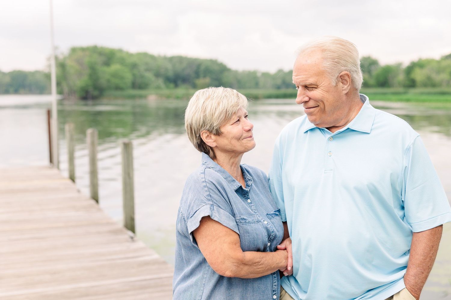 A couple shares an intimate moment while standing on a wooden dock by the water.