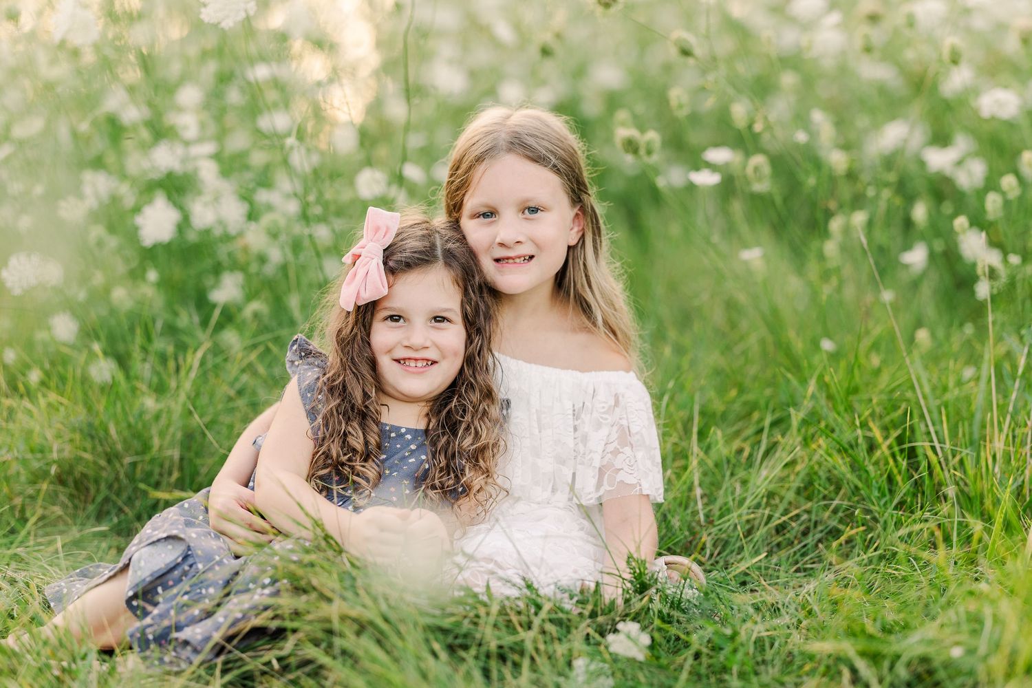Two figures share a sweet moment together while sitting in a blooming wildflower field.