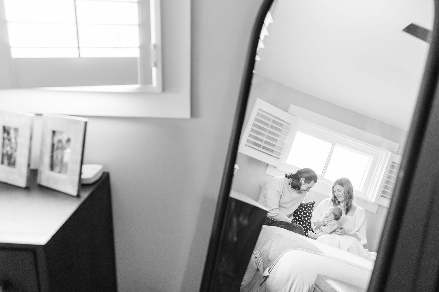 Parents sitting on their bed with their newborn baby reflected in a mirror during an in-home lifestyle newborn session in Palatine Illinois