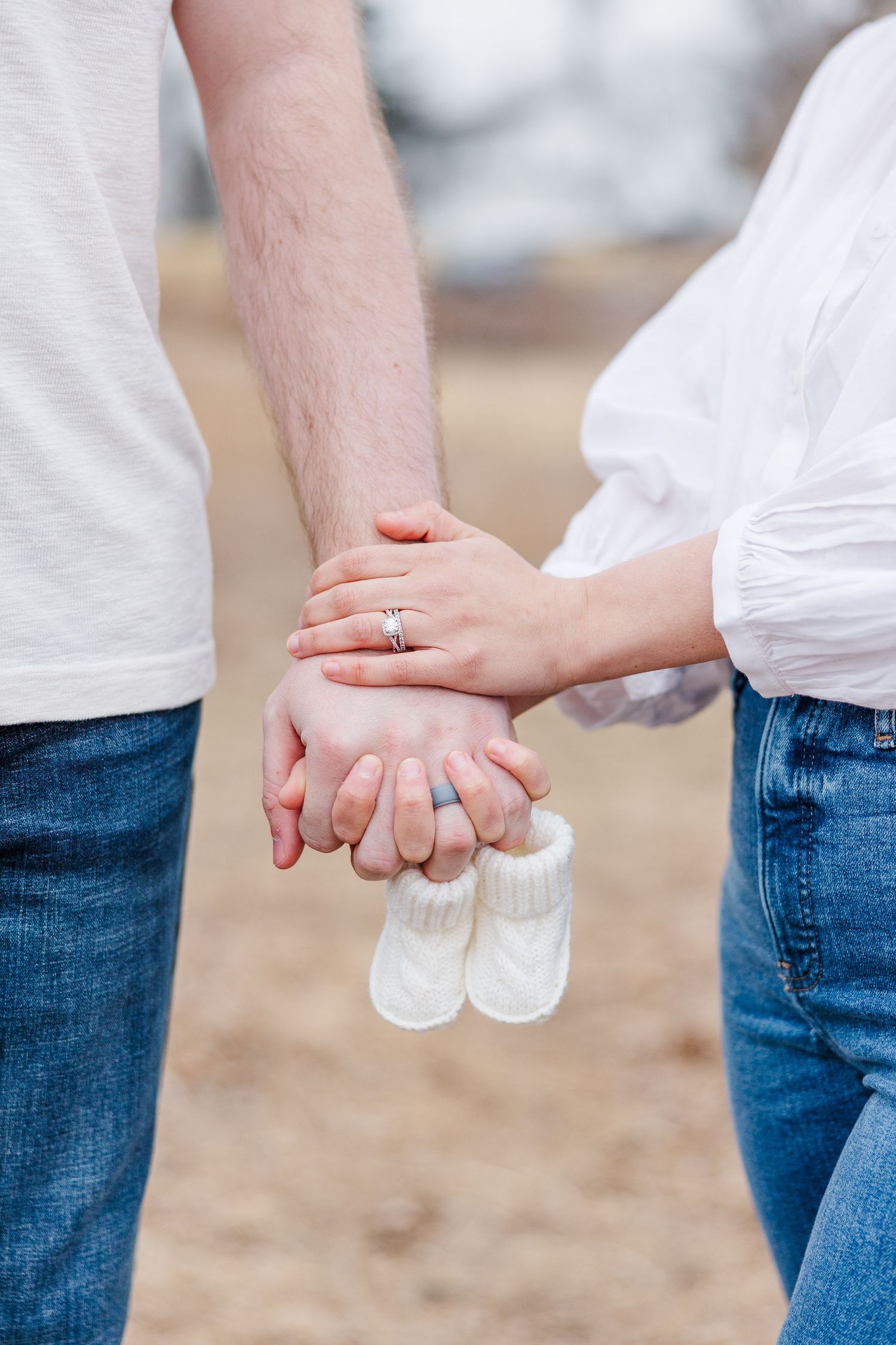 Pregnancy announcement detail of couple holding hands with baby shoes at Sands Main Street Prairie in Cary IL