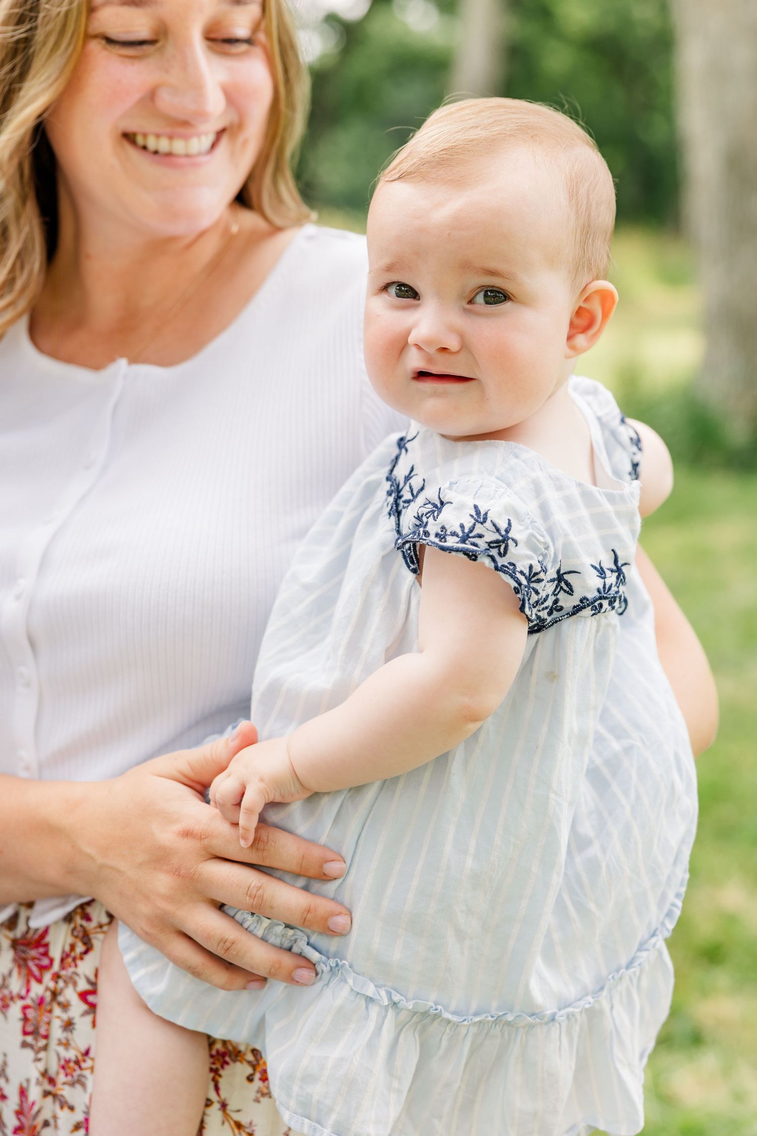 Mother holding baby girl in a white dress during a bright summer family photo session in Crystal Lake, Illinois.