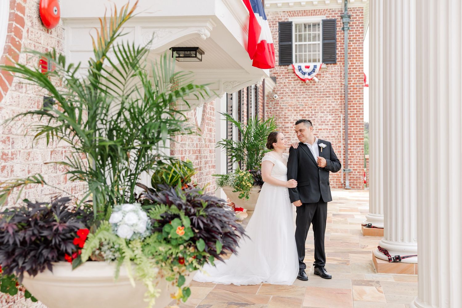 Bride and groom posing beneath the white columns and summer flowers at Cantigny Park’s McCormick House.