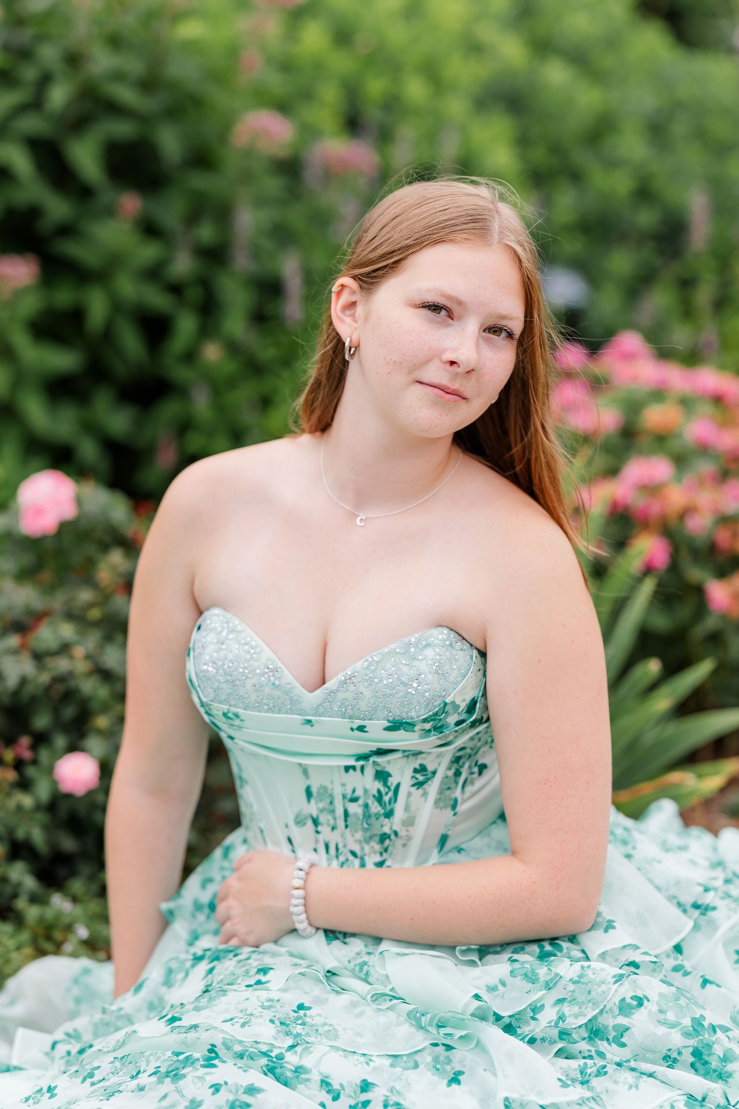 Samantha sits among pink flowers in a mint floral dress during her artistic senior portrait session.