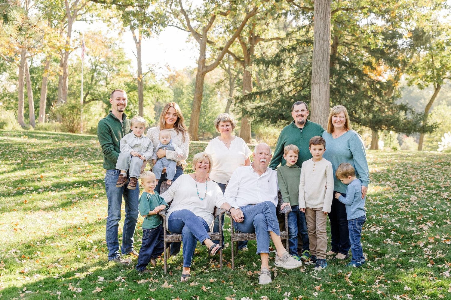 Multi-generational family portrait outdoors in a lush green park during autumn, smiling together for a professional photo.