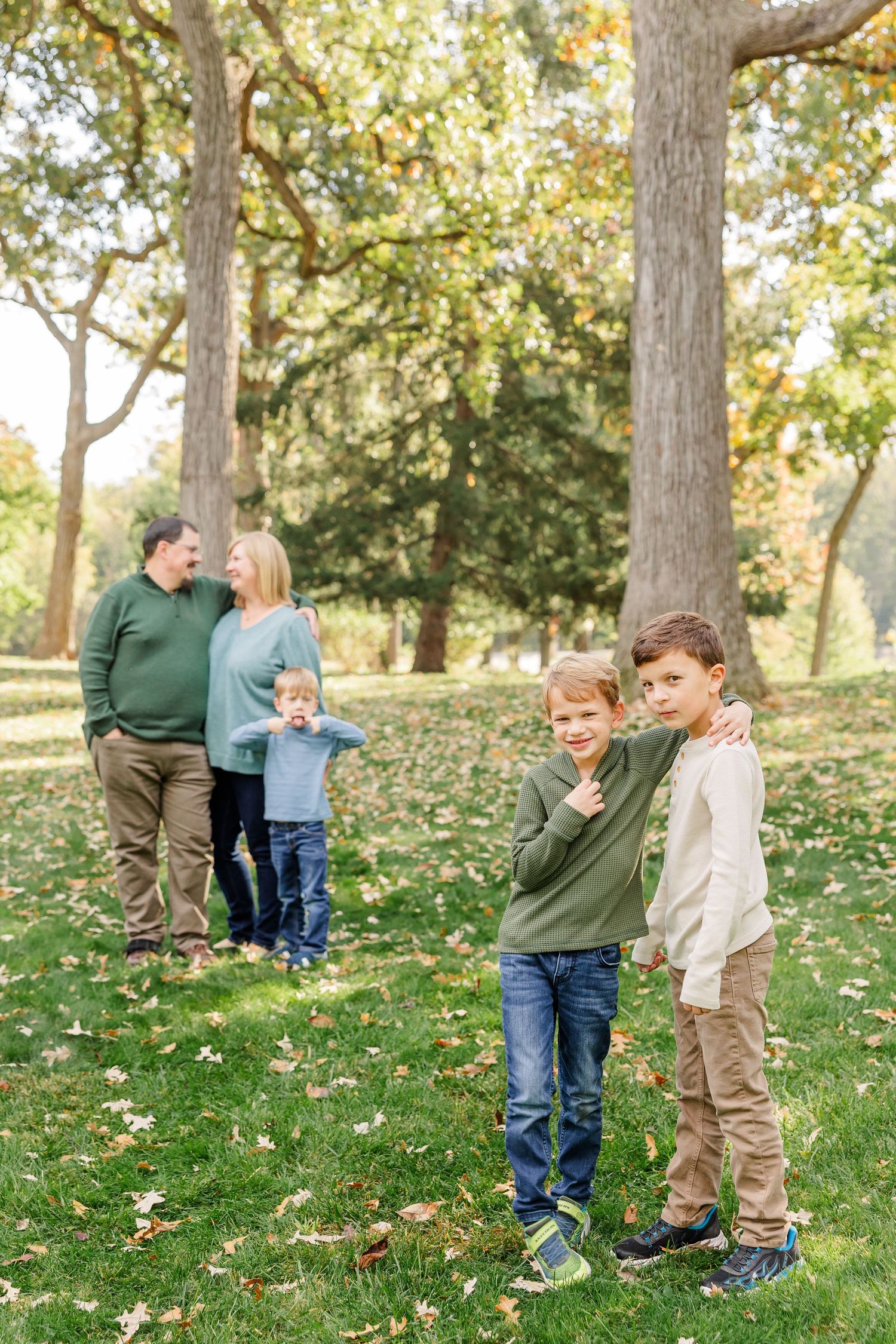 Family of five poses in a sunlit park with autumn leaves on the ground.