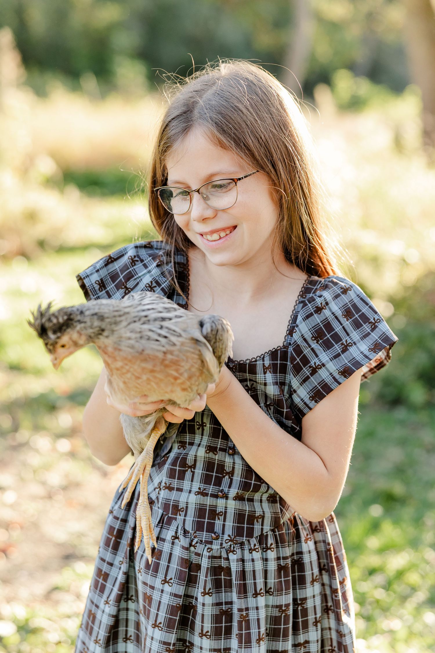 Girl in glasses smiling at a chicken she is holding during fall portraits in St. Charles, IL.