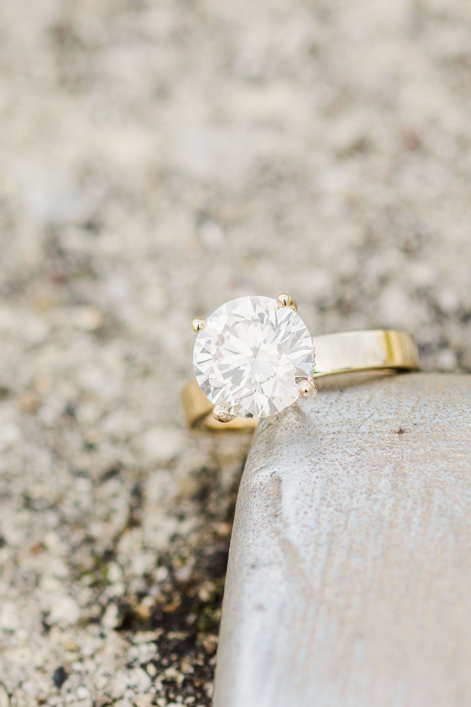 A stunning solitaire diamond engagement ring placed on a grey stone surface.