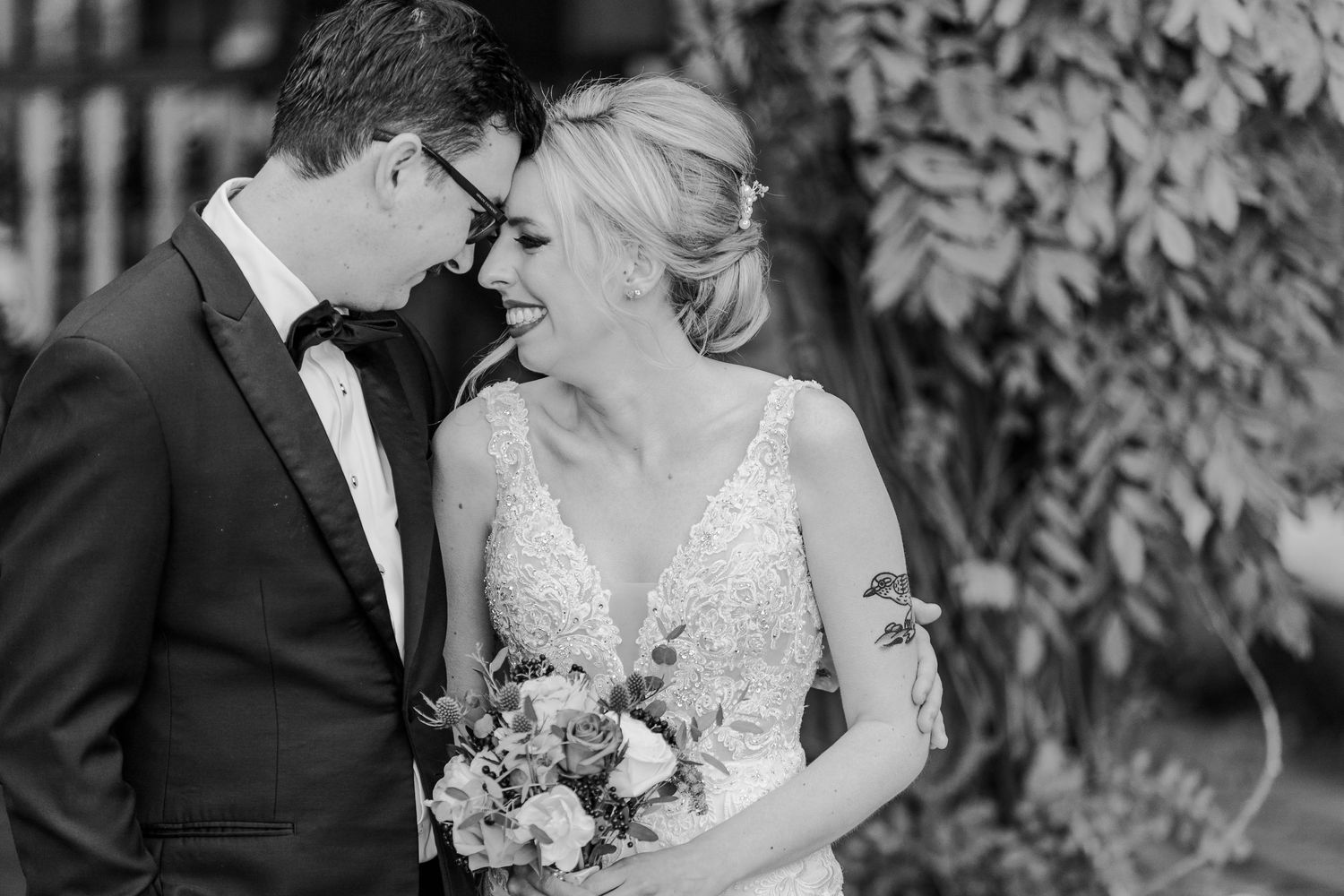A black and white portrait of newlyweds sharing an intimate moment in a garden setting.