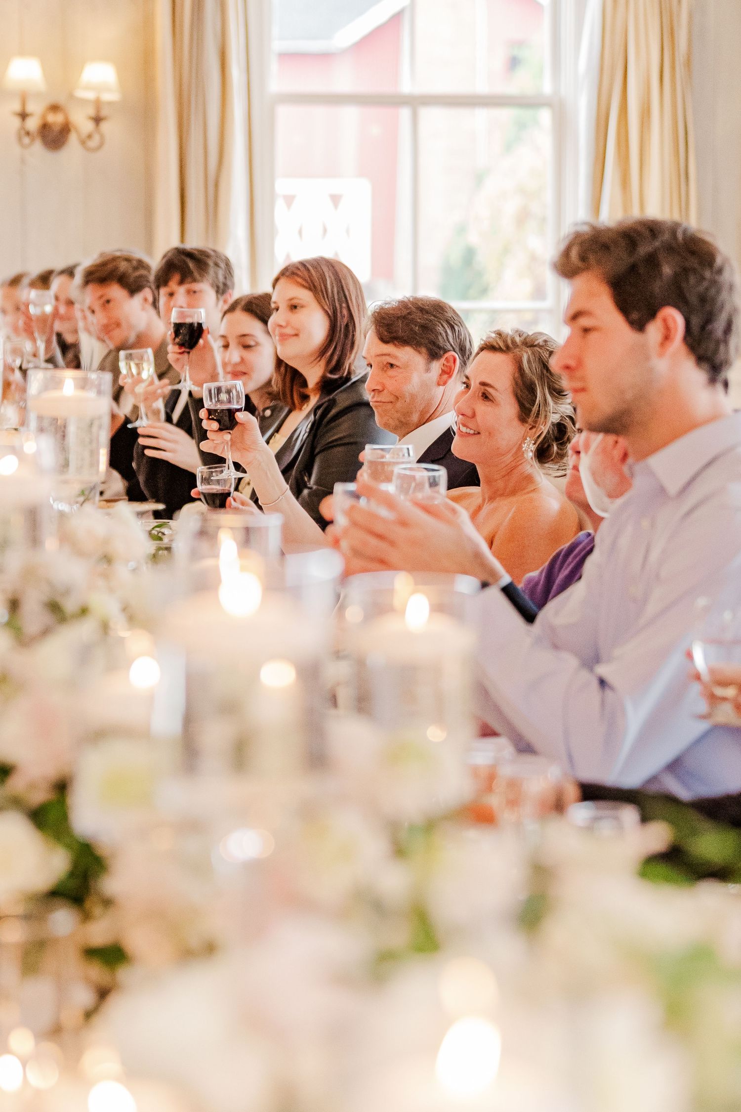 Wedding reception dinner scene with guests raising glasses for toast among floral centerpieces.