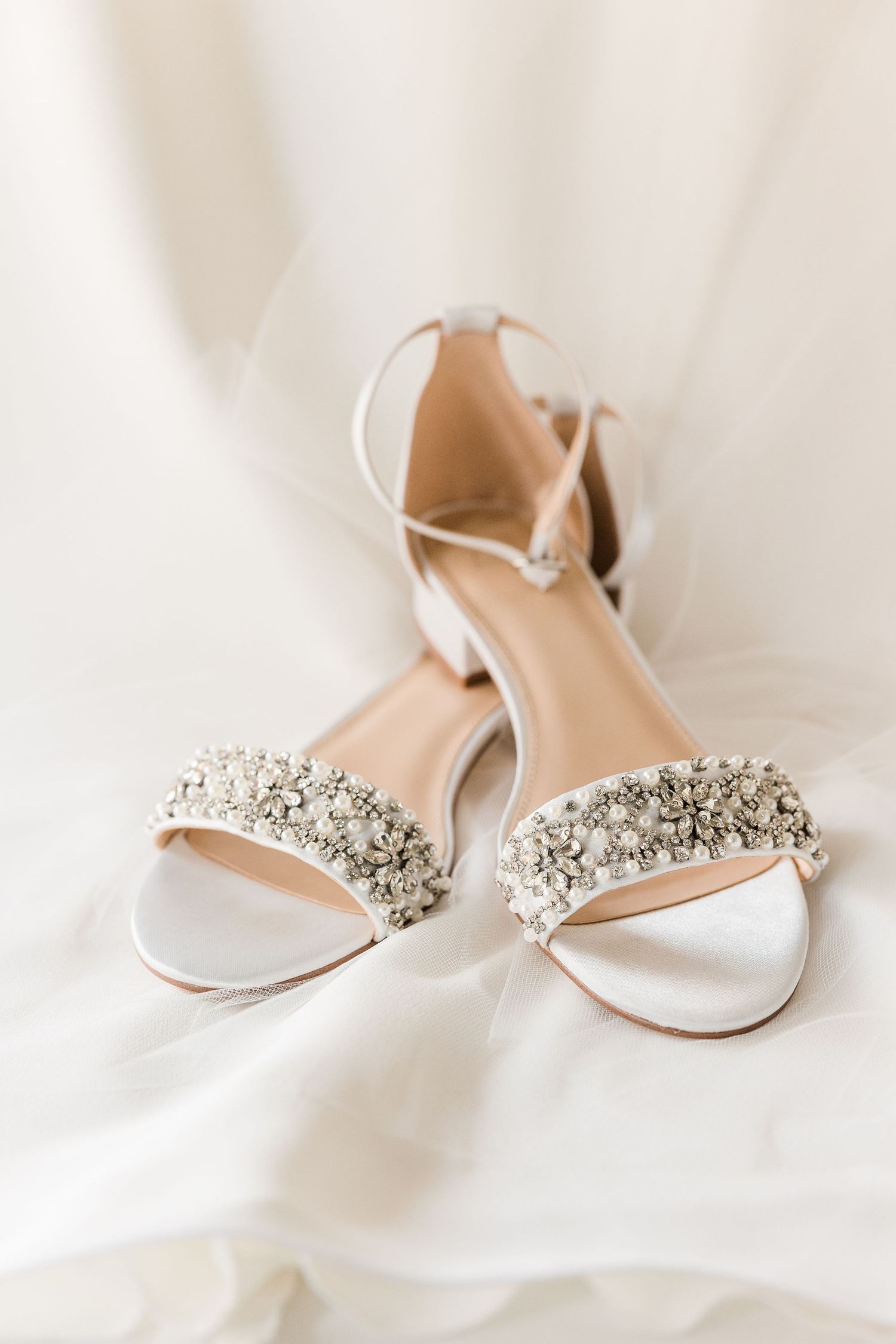 Elegant white wedding sandals with crystal-embellished straps on silk fabric.