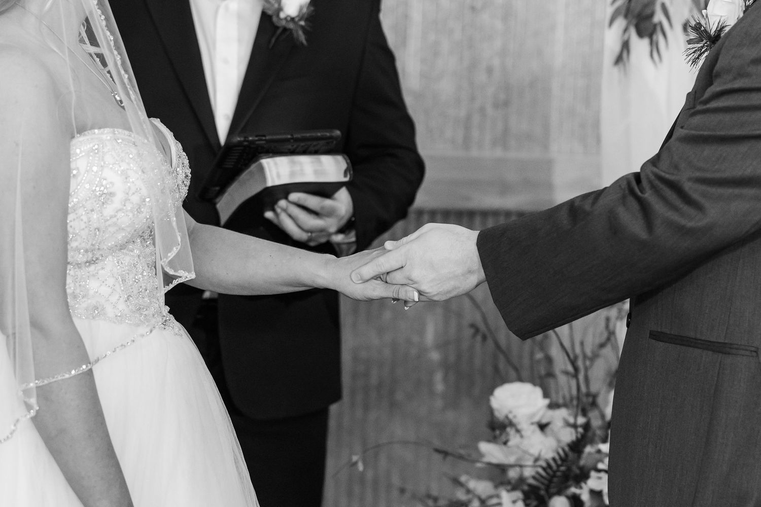 Black and white closeup of hands exchanging rings during a wedding ceremony.