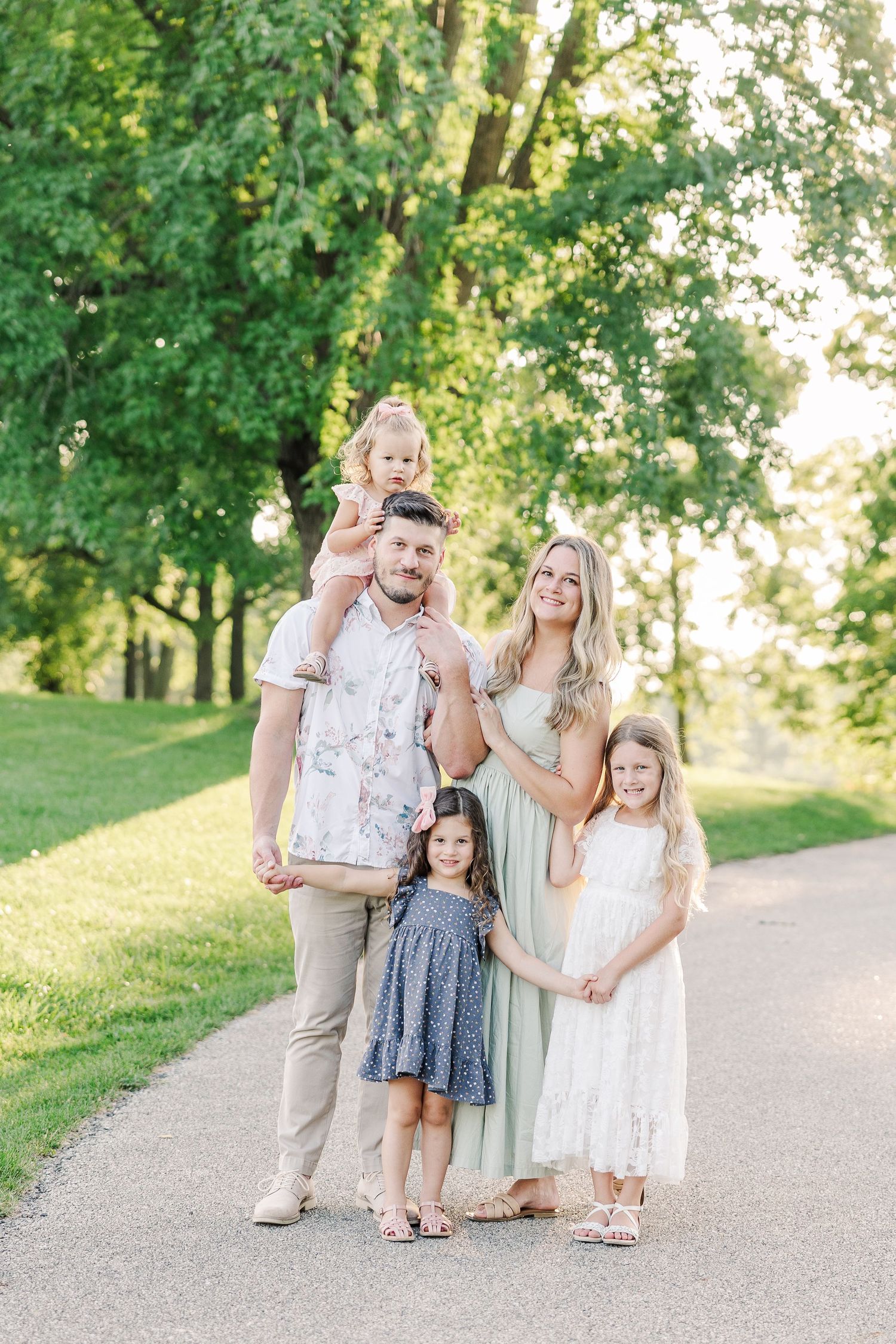 A family in coordinated outfits poses together on a tree-lined path during golden hour.