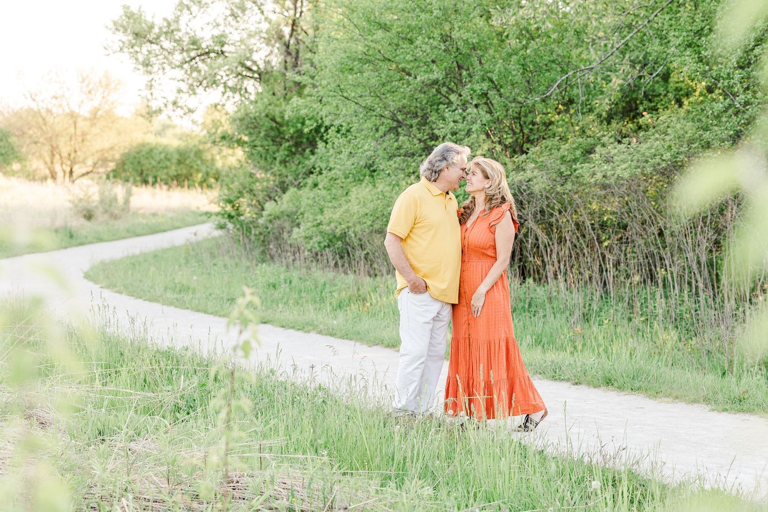 Couple walking together on a sunlit path surrounded by greenery.