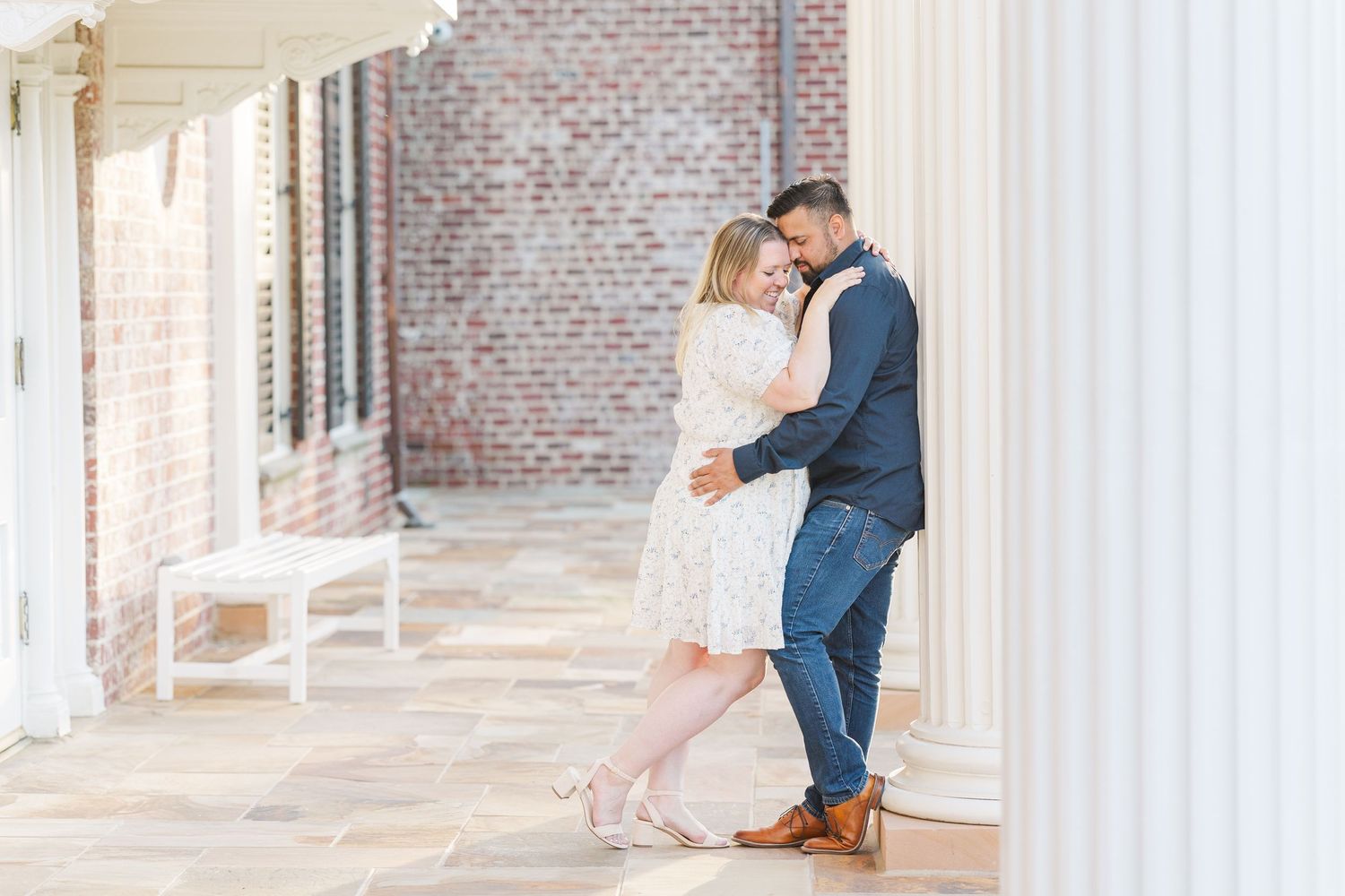 Intimate portrait by white columns and brick walls during golden hour.